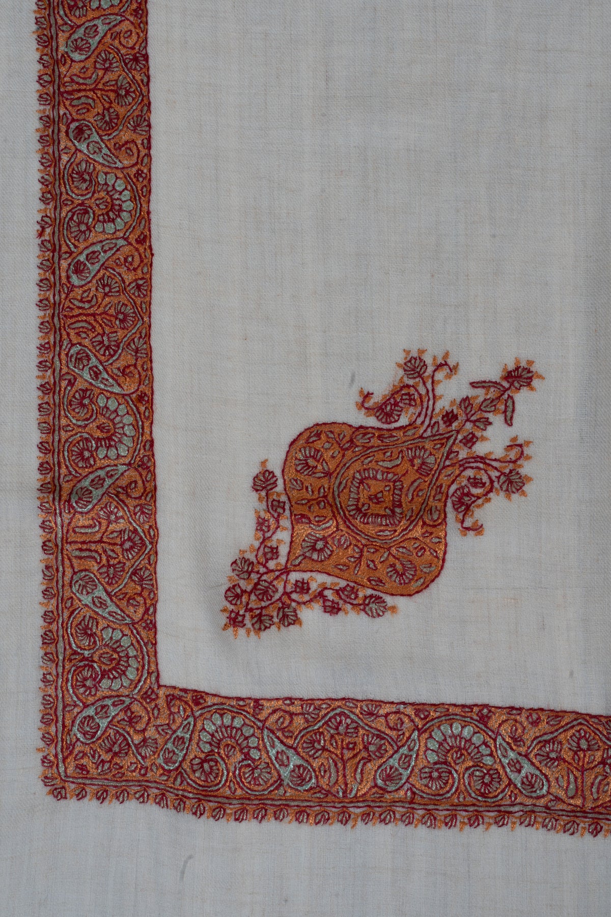 Ivory rumal corner with a burnt-orange floral motif beside a Sozni border of copper and sage curling paisleys