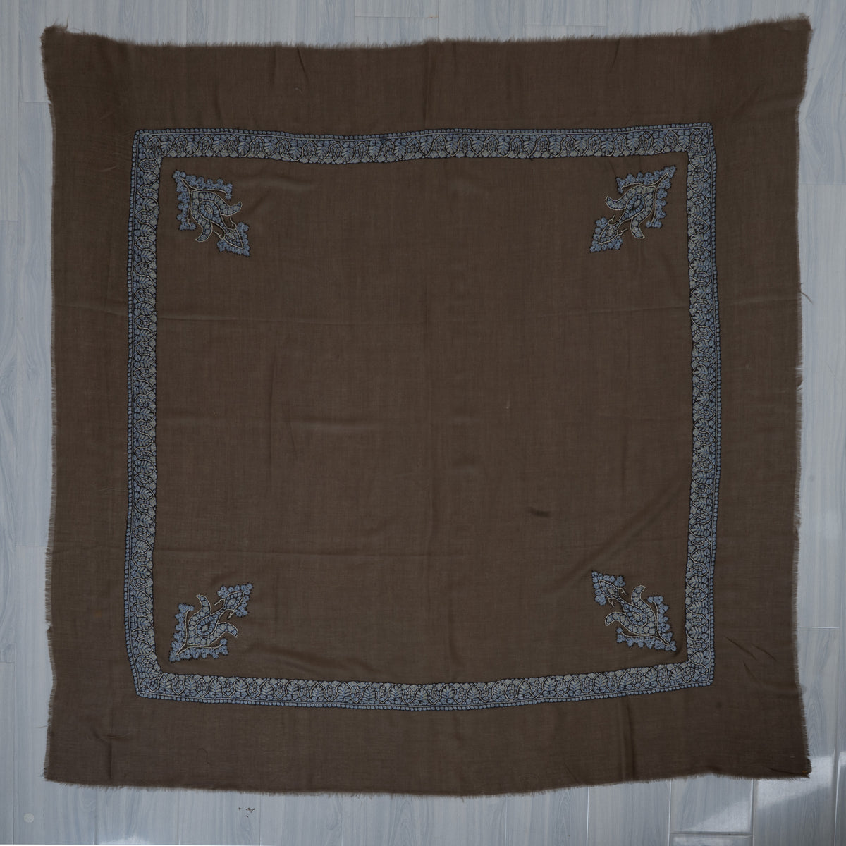 Mocha-brown cashmere rumal laid flat, with a square pale blue border and four matching corner motifs