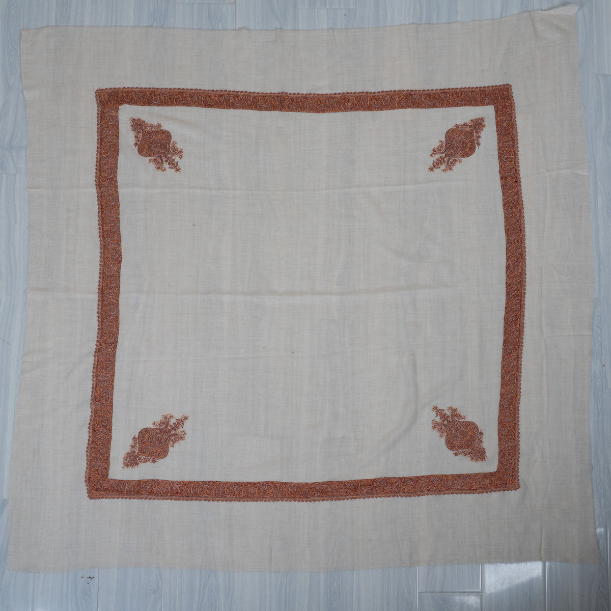 Cream cashmere rumal laid flat, with a square copper-rust border and four matching corner motifs