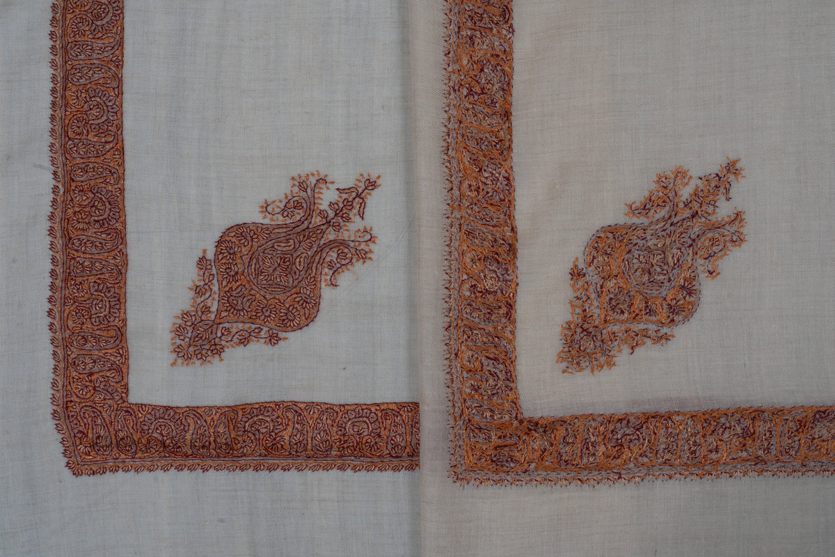 Overlapping cream rumal corners showing the front and reverse of copper-rust embroidery