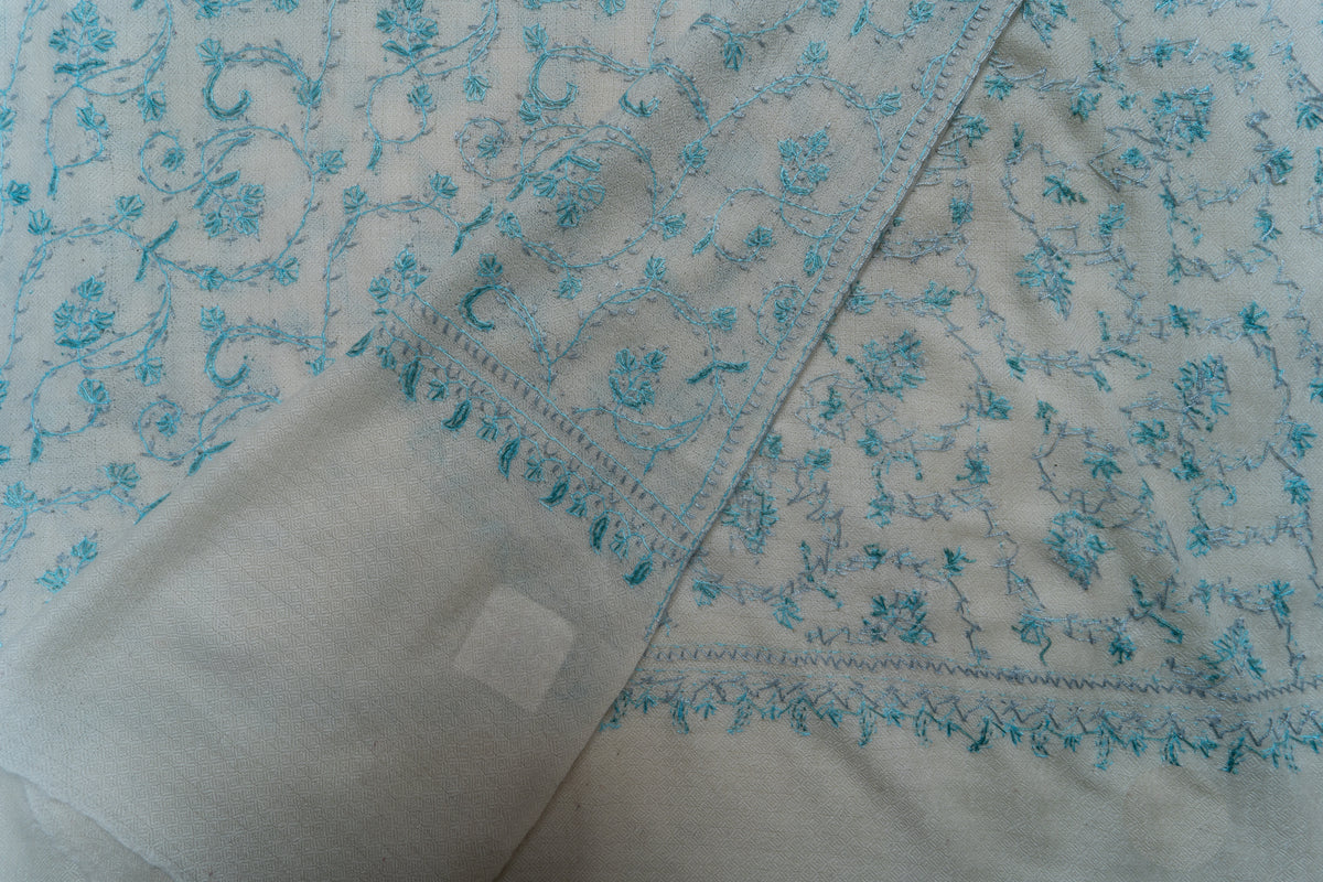Folded corner of the white stole showing both faces of the pale blue floral embroidery and a plain end panel.