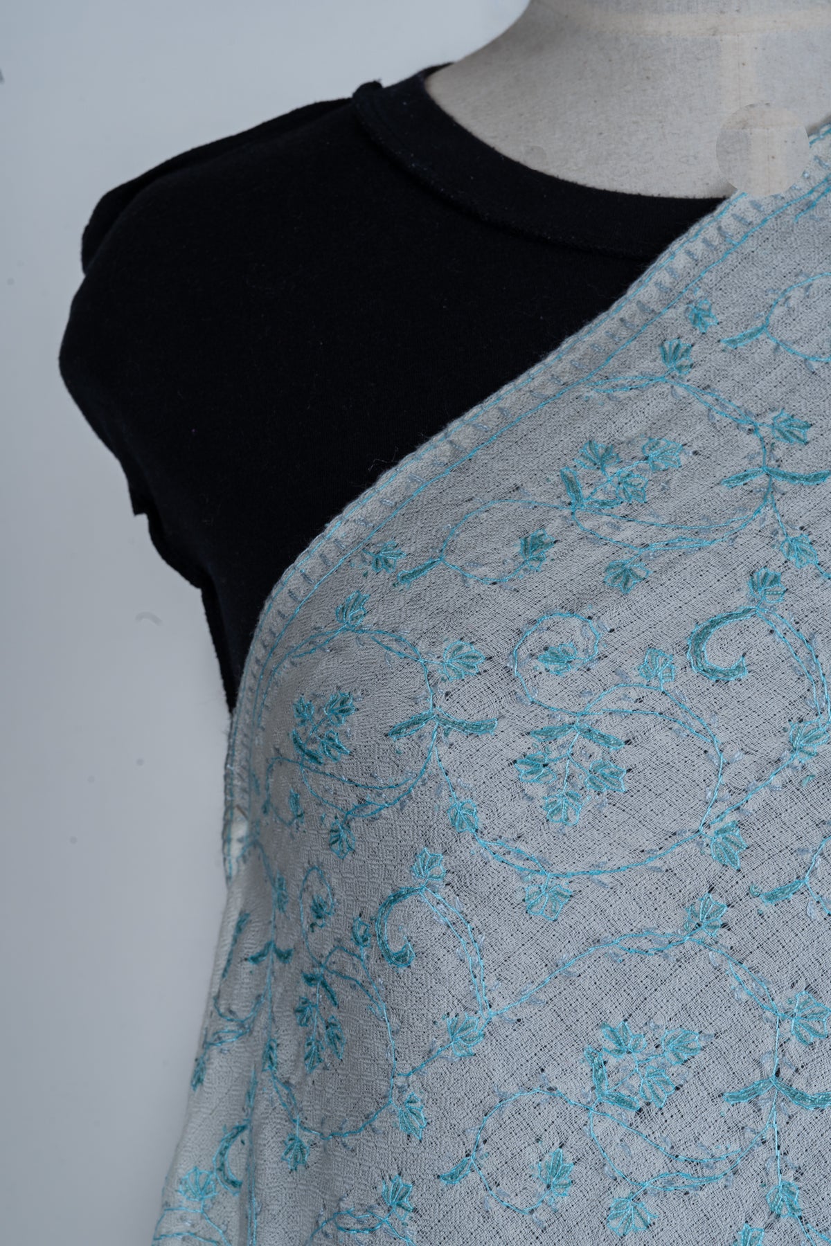 Shoulder close-up of the white stole showing pale blue floral vines and a narrow embroidered edge.
