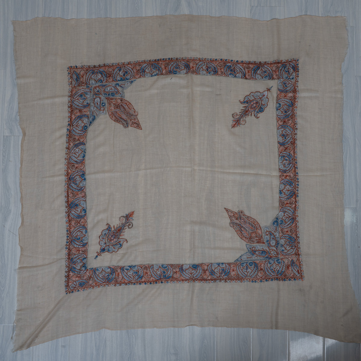 Square beige rumal laid flat with coral and blue leaf borders, two large corner panels, two small paisleys and a plain centre