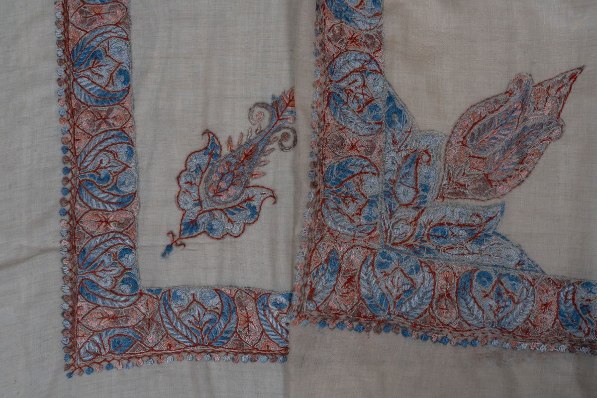 Folded beige rumal showing both sides of coral and powder-blue Sozni borders, a small paisley and a large leaf arrangement
