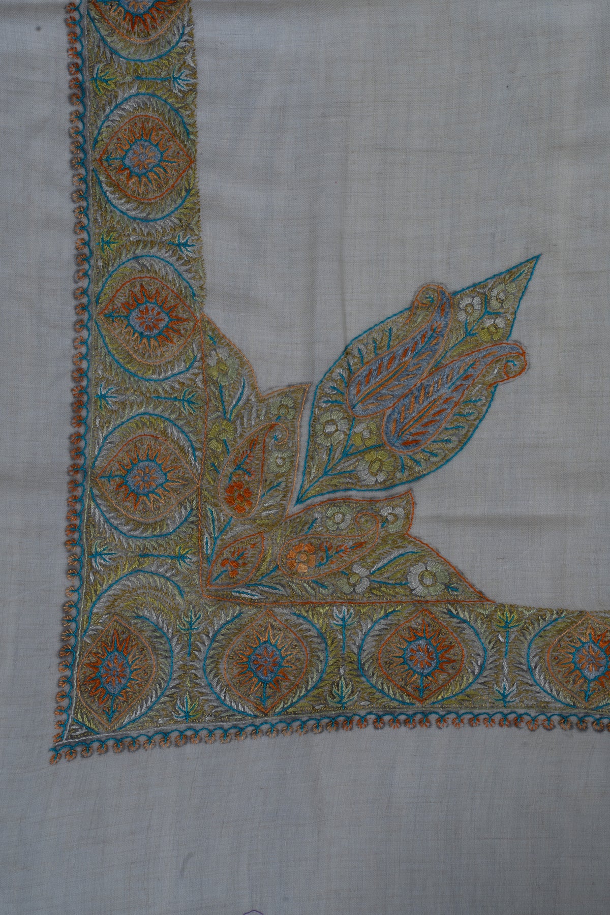 Amber and blue Sozni leaves rise from a circular medallion border at the corner of a pale cashmere rumal.