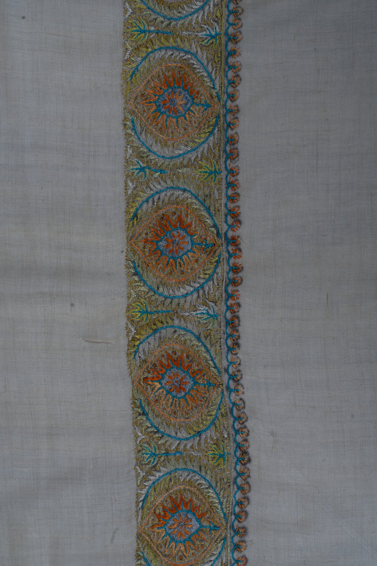 Close-up of circular Sozni floral medallions in amber, blue and muted green along a pale cashmere rumal border.