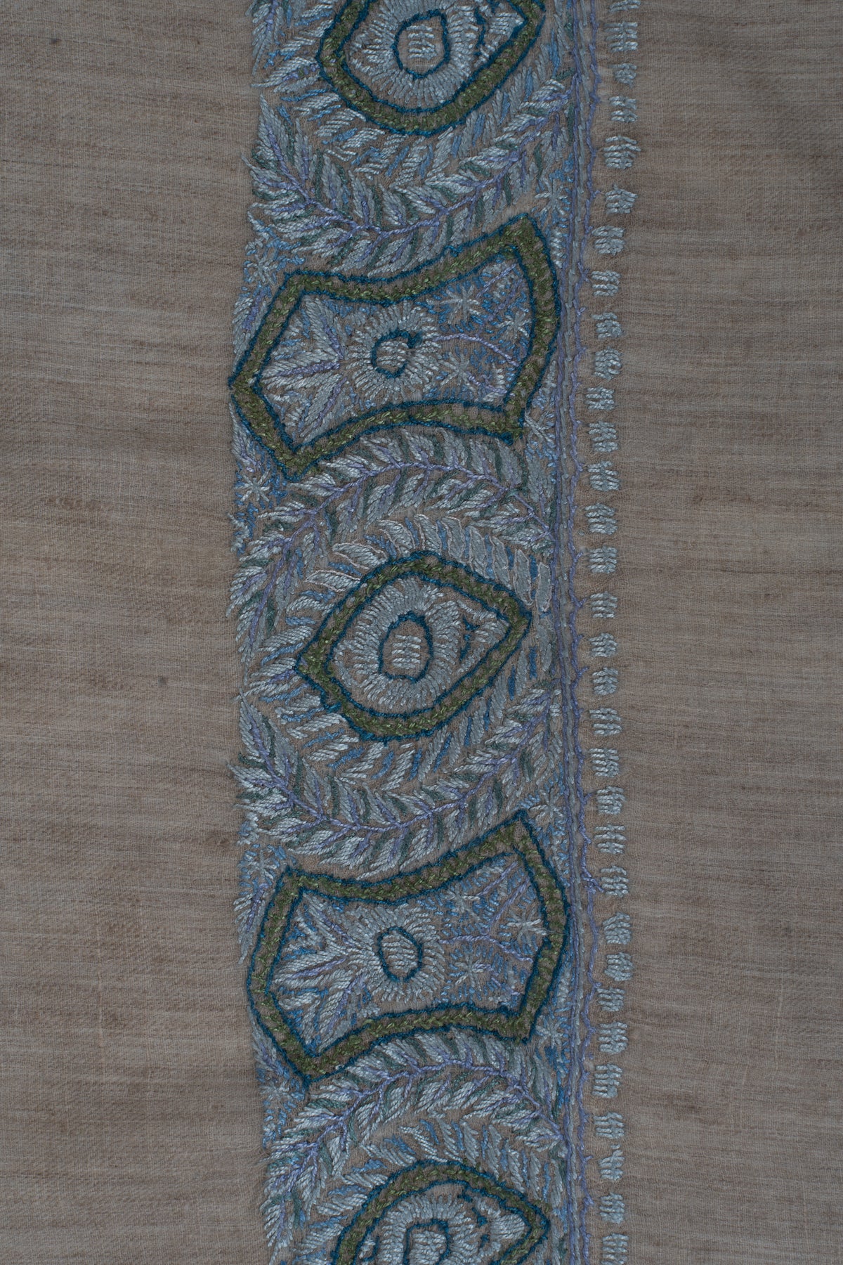 Close-up of blue and sage geometric motifs surrounded by fine leaf embroidery along the rumal's border