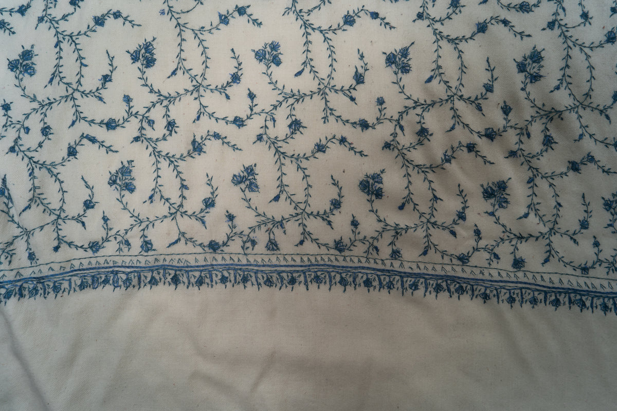 Close-up of blue flowers and curling leafy vines above the ivory stole’s narrow end border and plain panel