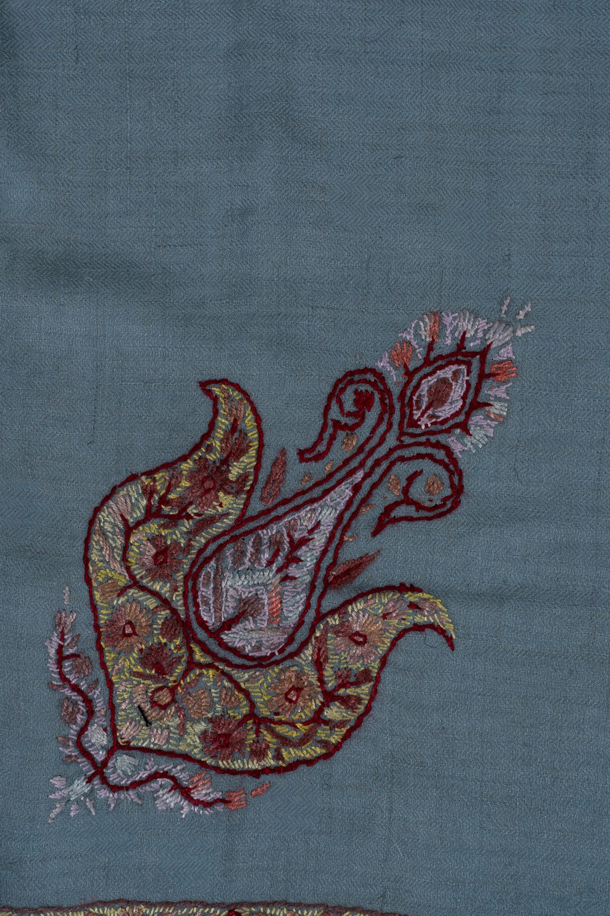 Close-up of a garnet-outlined Sozni paisley with pale-blue and gold floral details on sky-blue cashmere.