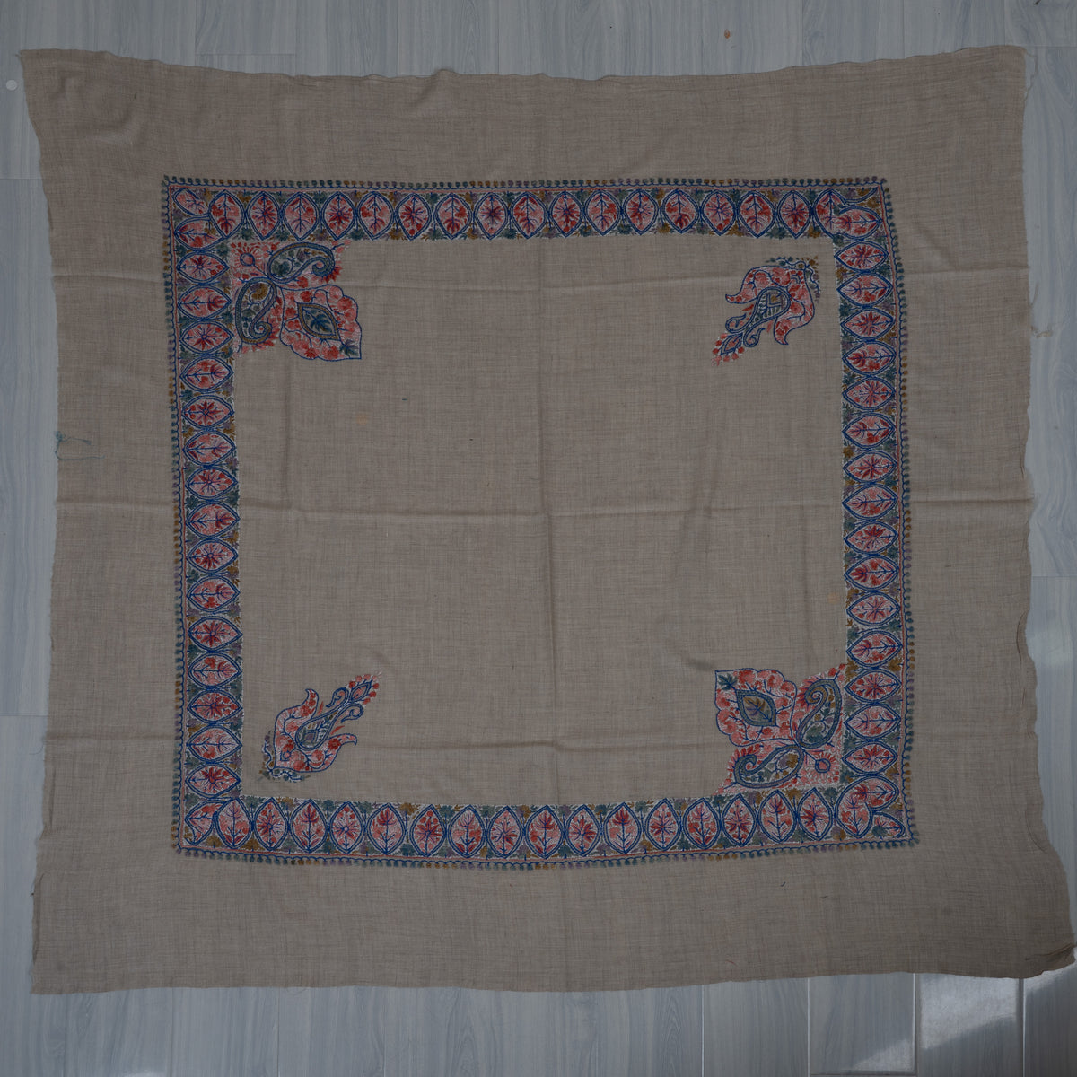 Square beige rumal laid flat with coral and blue leaf borders, two large corner panels, two small paisleys and a plain centre