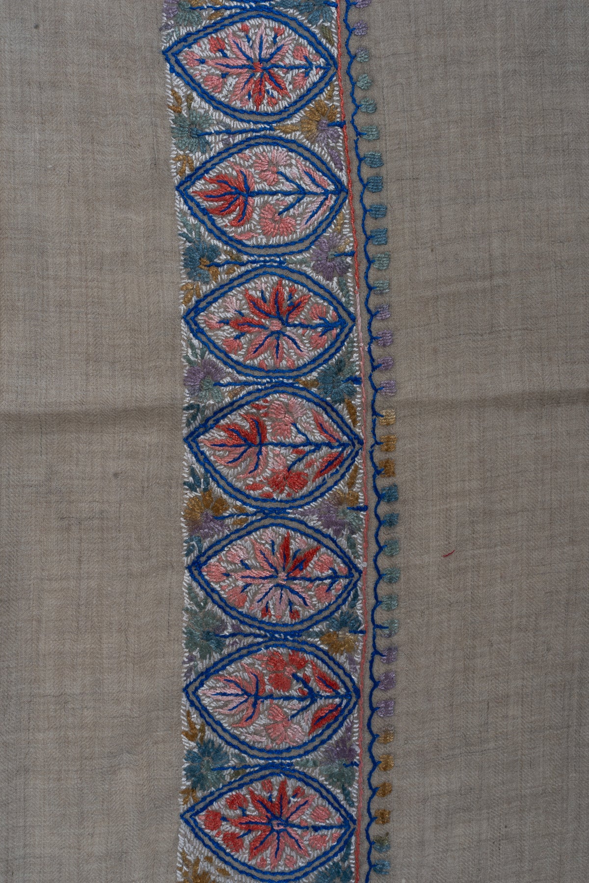 Close-up of coral Sozni leaf medallions outlined in deep blue with sage and golden accents along a beige rumal border