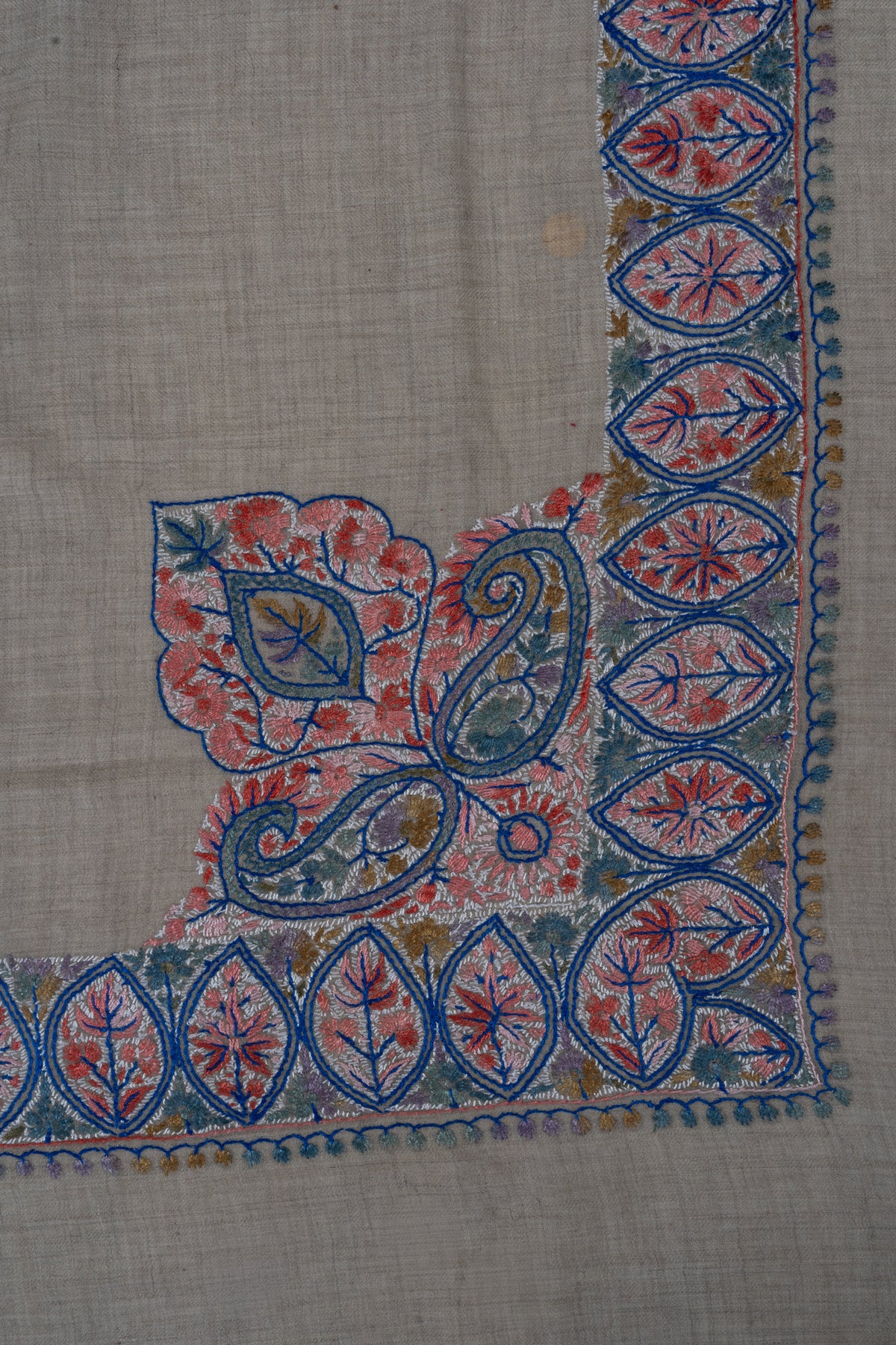 Beige rumal corner with a large coral and blue Sozni leaf-and-paisley arrangement connected to the border