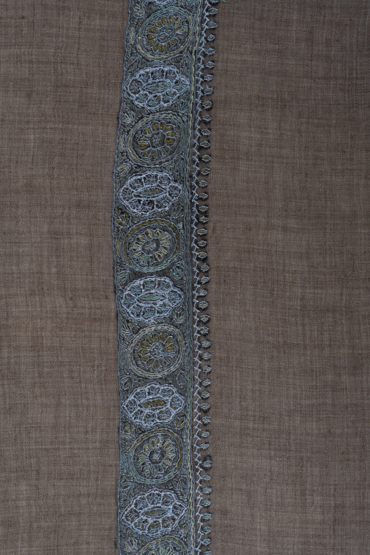 Close-up of a blue-grey Sozni border with circular floral medallions and pale leaf edging on mushroom-brown cashmere.