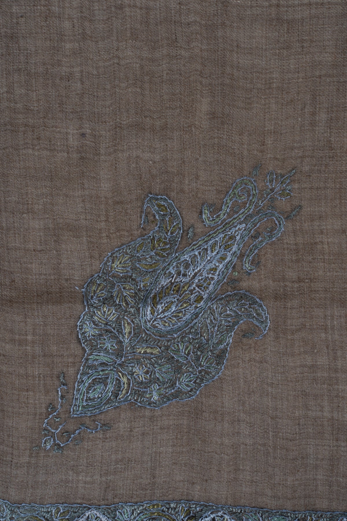 Close-up of a blue-grey Sozni paisley filled with pale floral and leaf stitching on mushroom-brown cashmere.