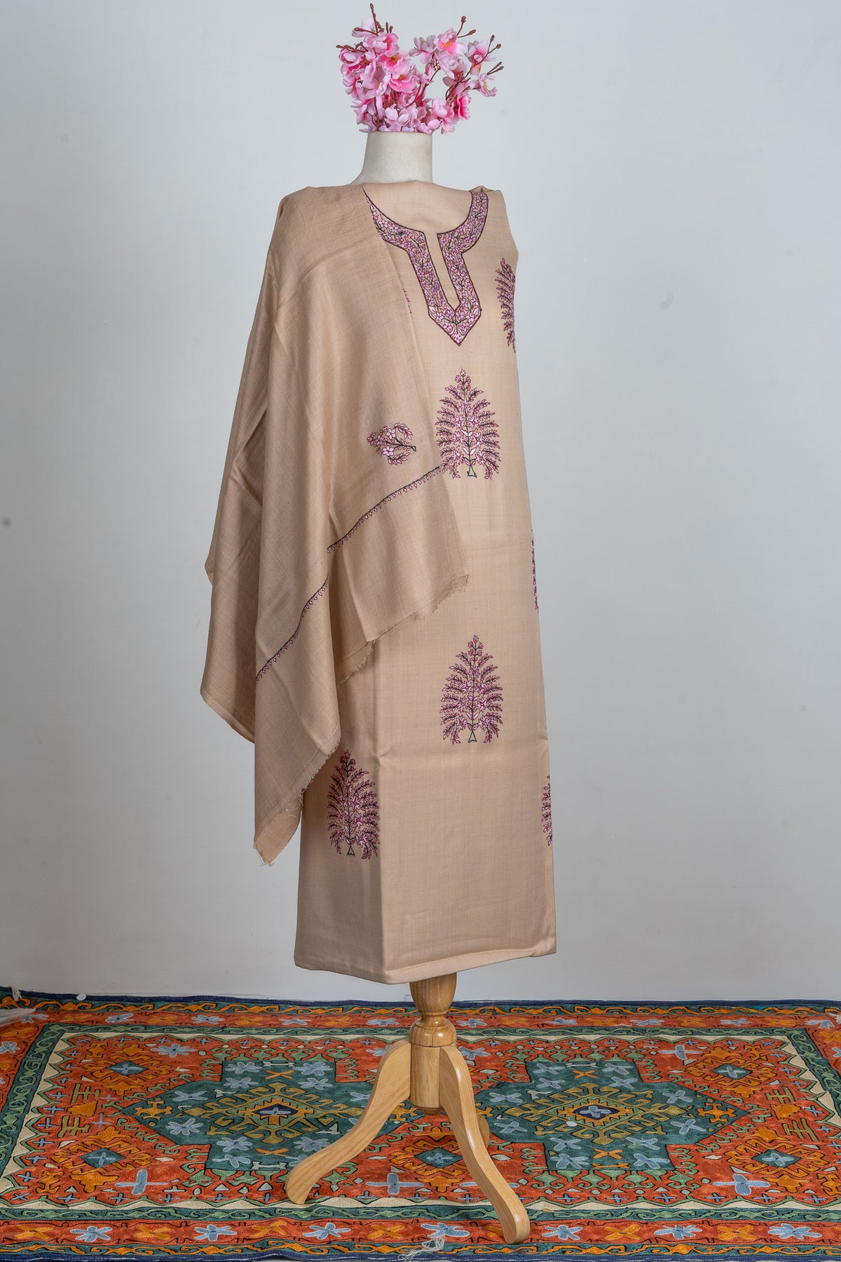 Sand-beige suit fabric and matching dupatta on a mannequin, with rose-pink neckline embroidery and tree motifs
