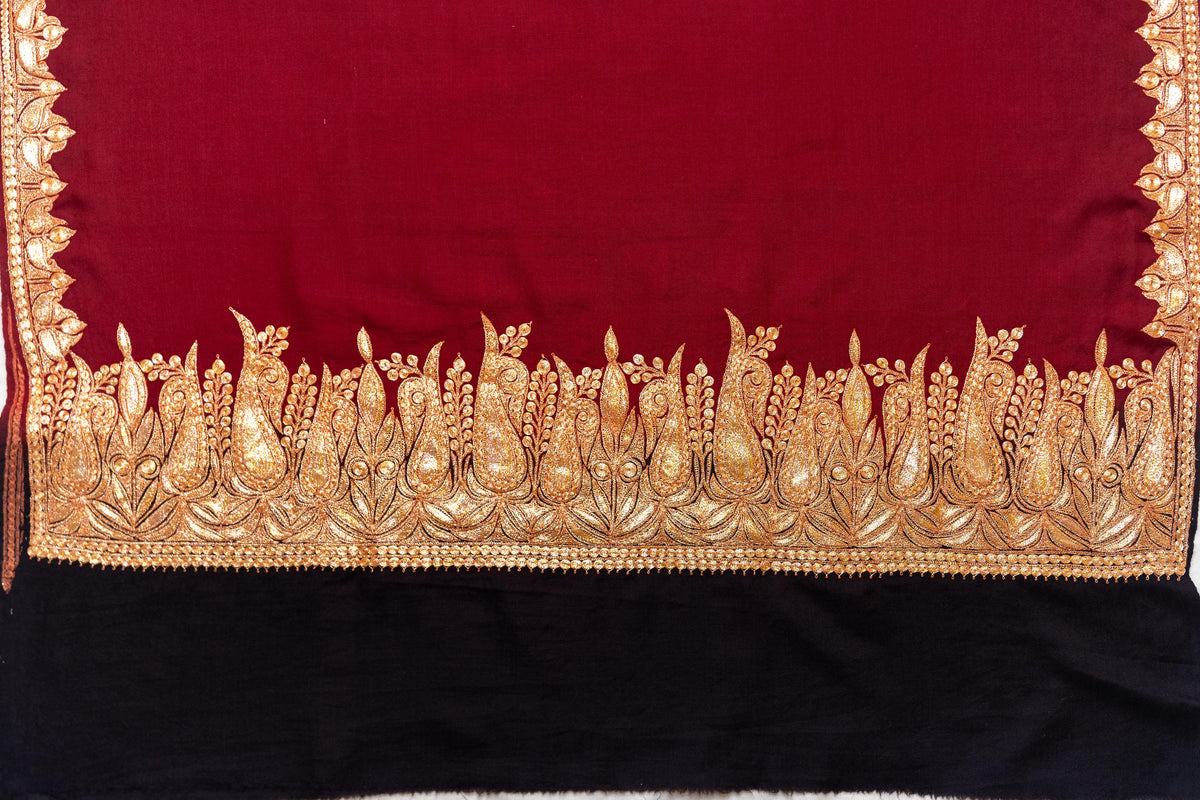 Crimson shawl spread flat, showing its gold-coloured paisley and leaf border above a broad plain black end panel.