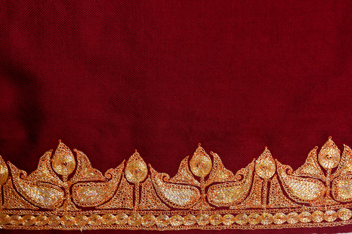 Flat close-up of the crimson shawl side border with repeating gold-coloured leaves and upright buds.