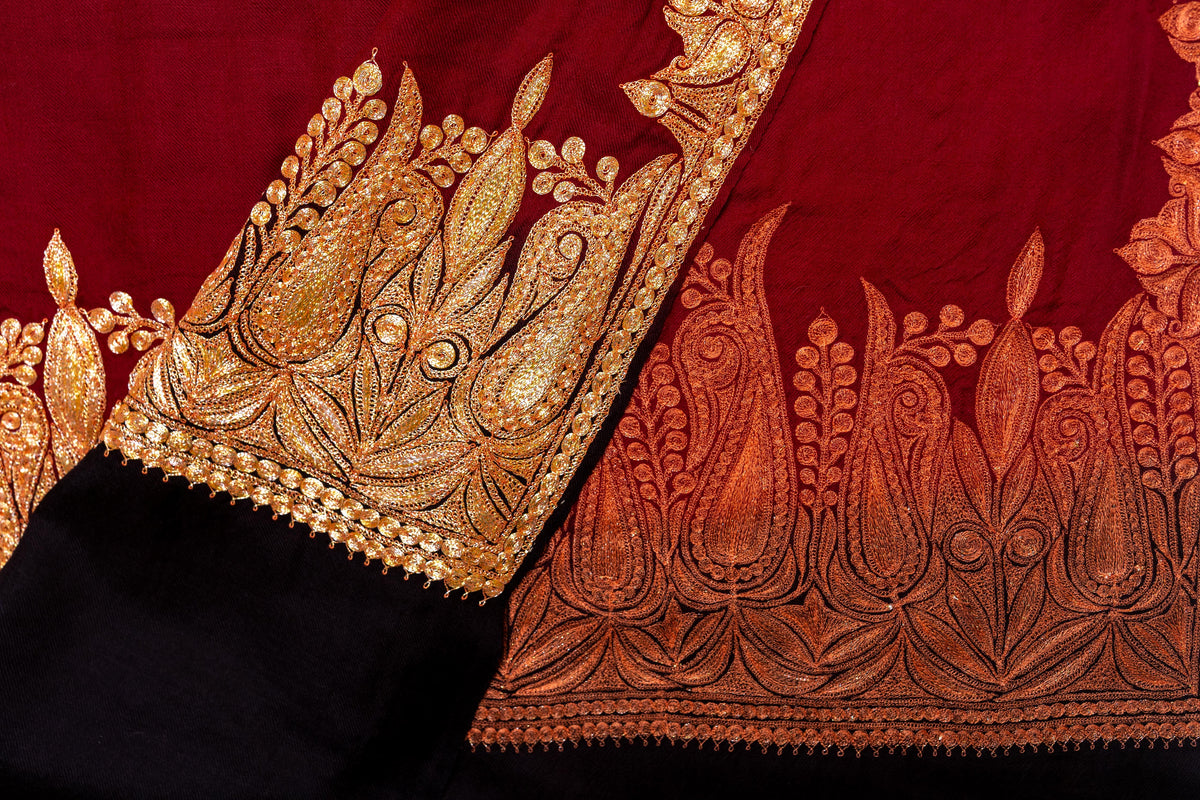 Overlapping shawl corners showing the bright gold-coloured embroidered face and orange reverse stitching above black ends.