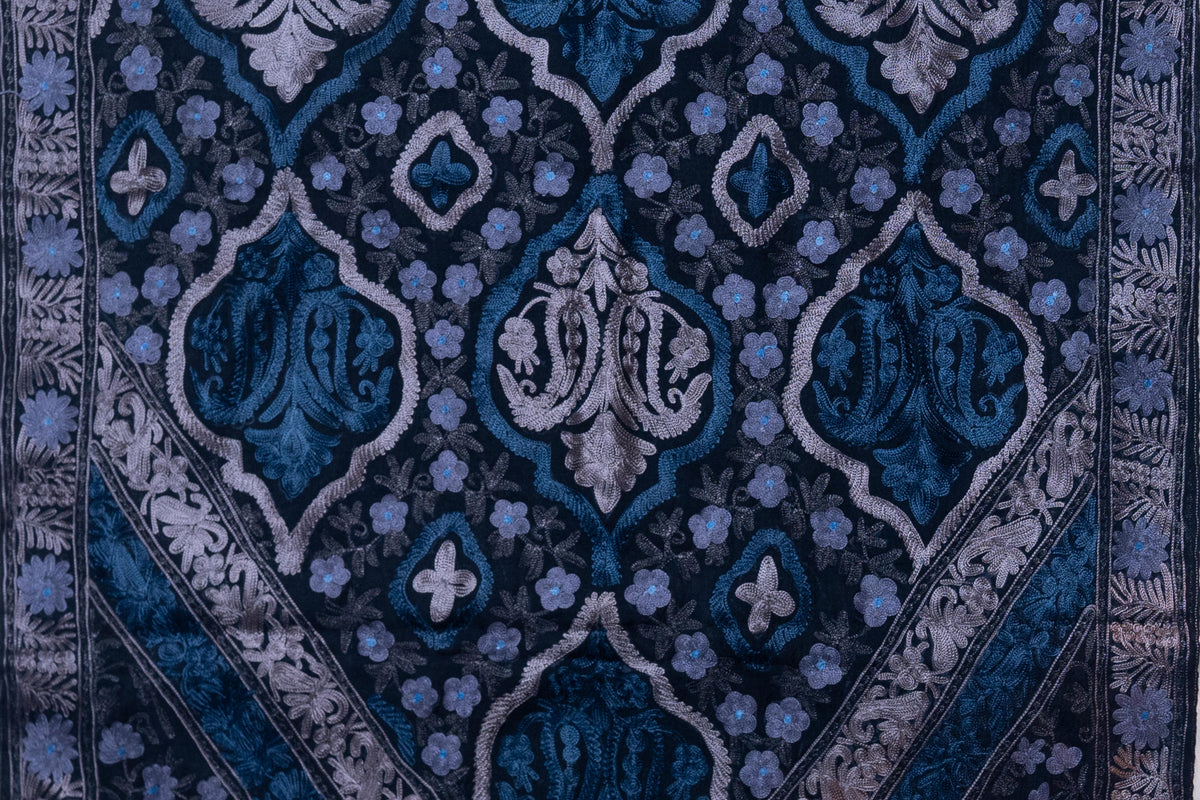 Flat view of large blue and silver-toned floral medallions among small blue flowers on black wool