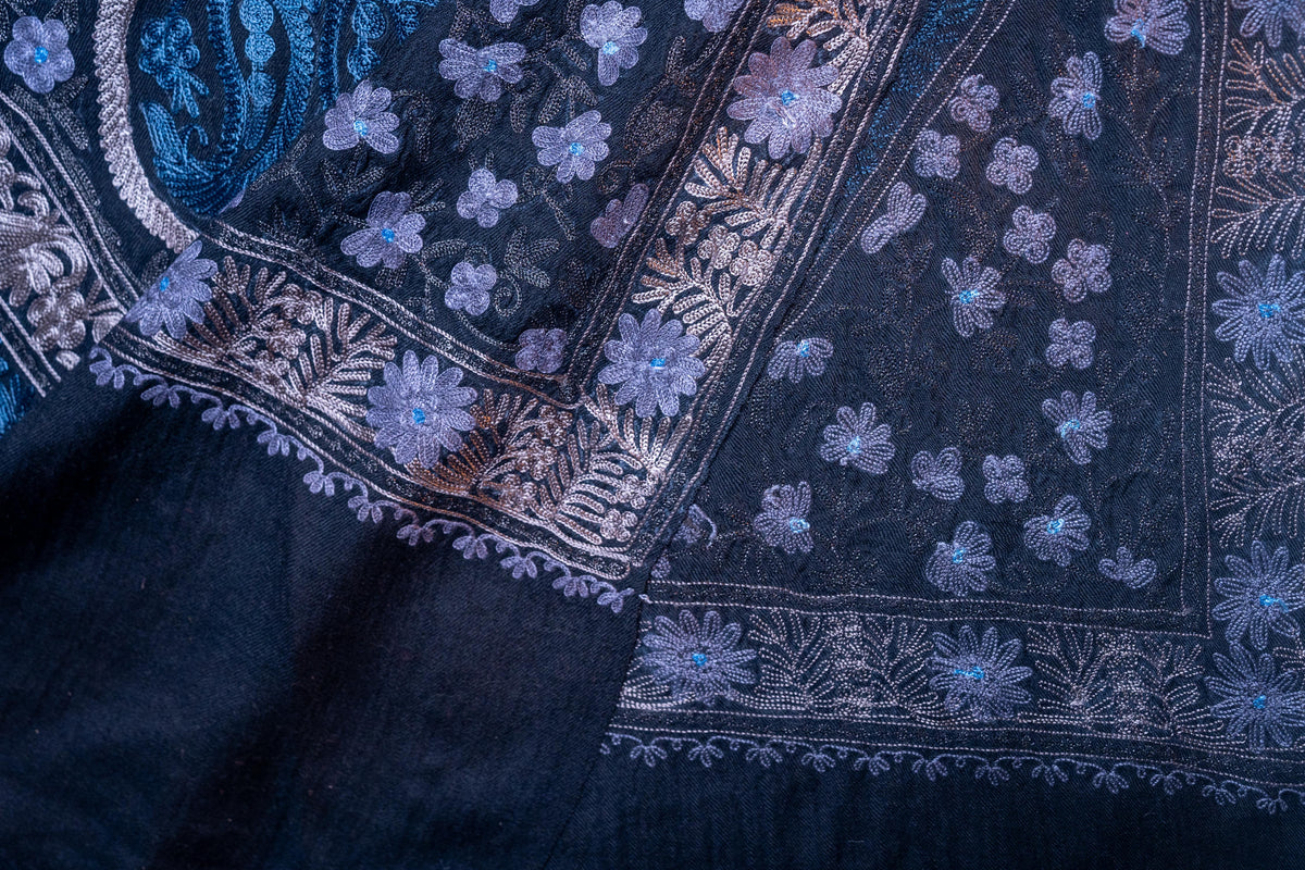 Folded black stole corner showing blue and silver-toned floral borders and the reverse stitching beneath