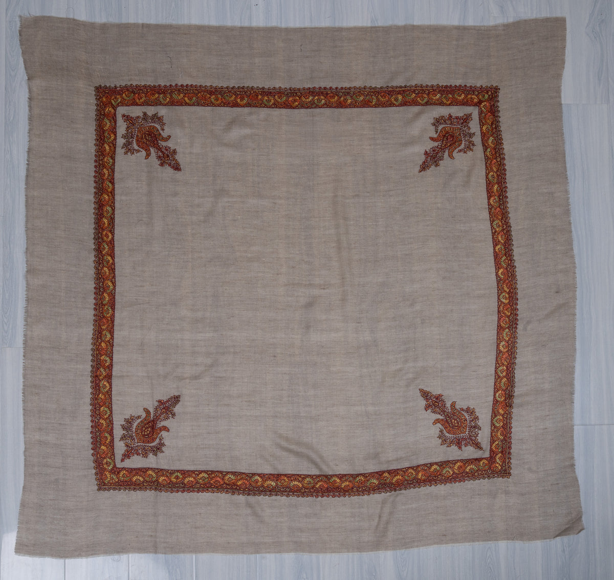 Taupe cashmere rumal laid flat with a colourful floral Sozni border and four corner paisleys around a plain centre