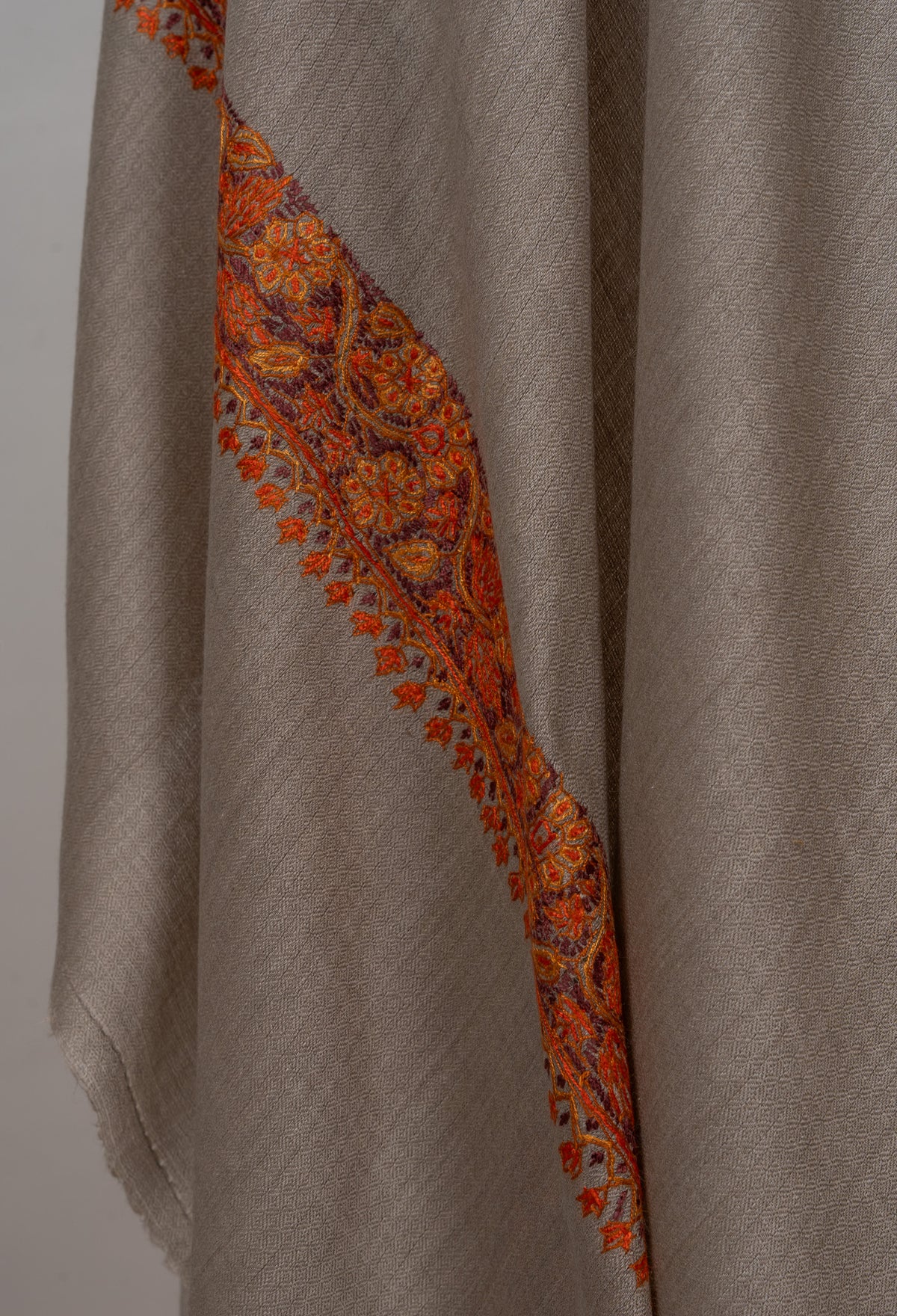 Hanging edge of a grey-beige shawl, showing the orange-red Sozni floral border and small pendant motifs