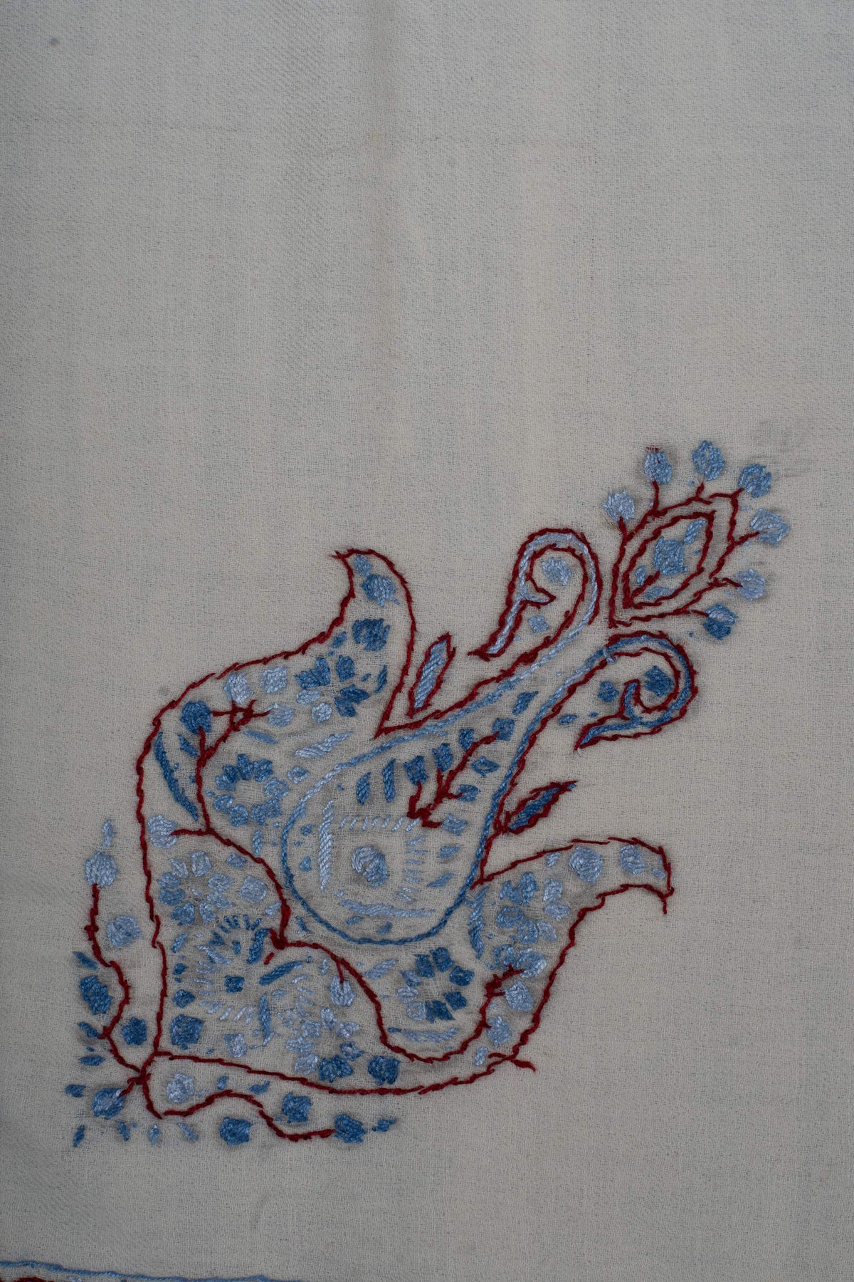 Close-up of a blue Sozni paisley with burgundy outlines and pale floral details on ivory Merino wool.