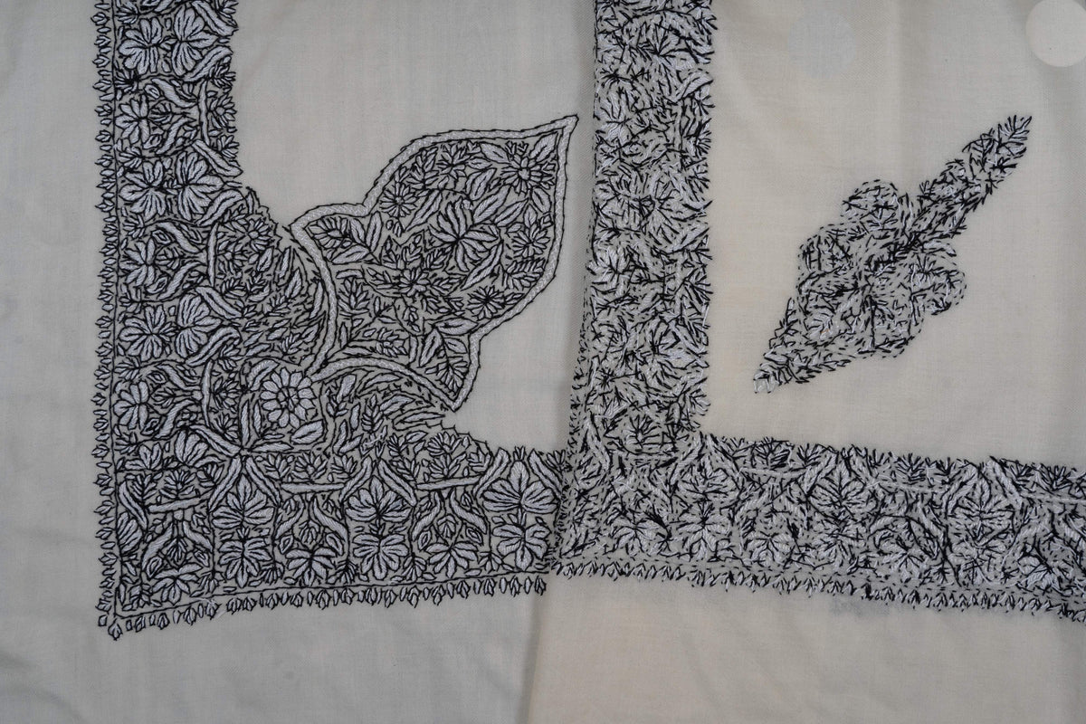 Overlapping ivory rumal corners showing a dense black Sozni floral border and two differently shaped corner motifs