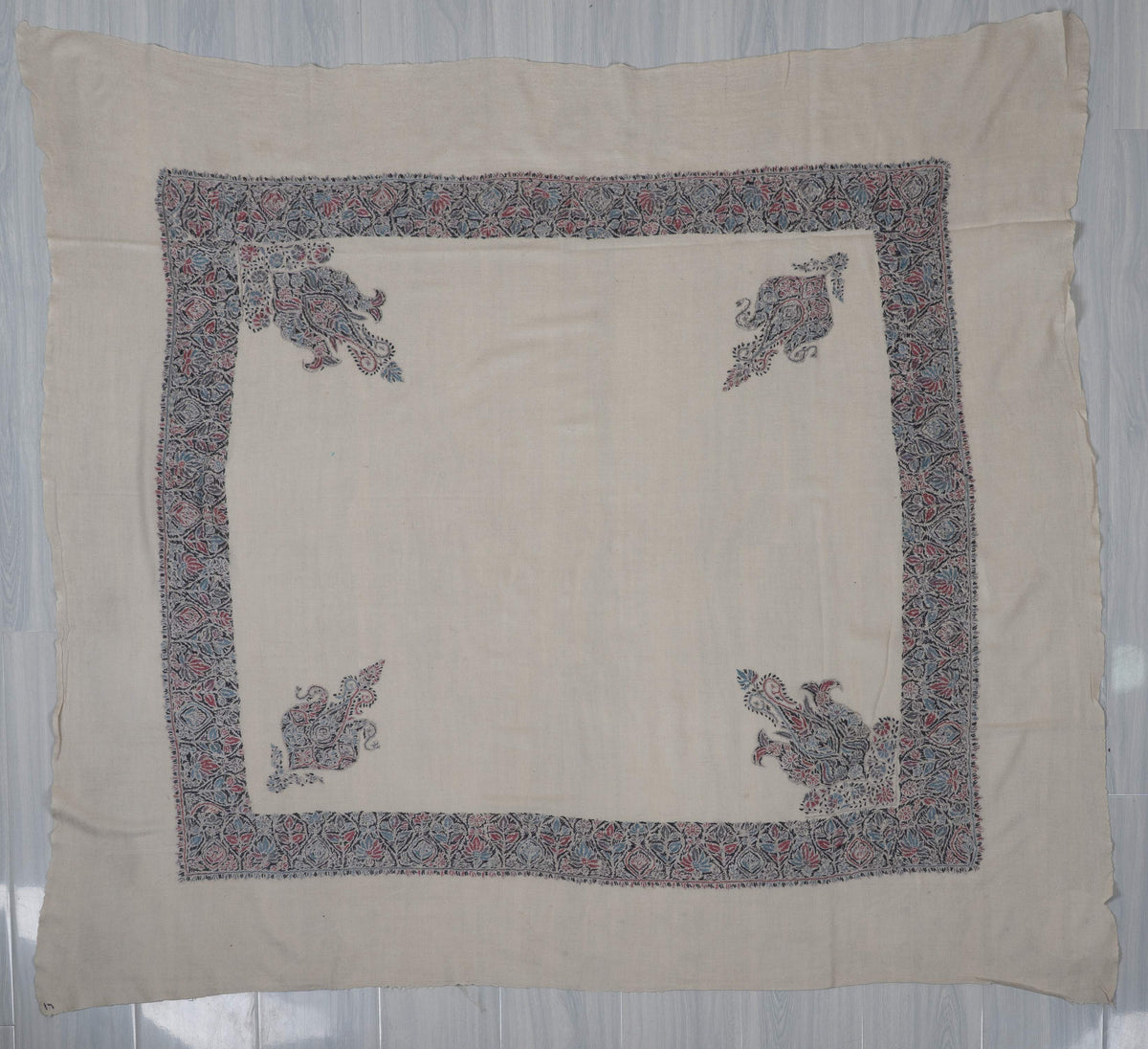 Ivory Merino rumal laid flat, with rose-blue floral borders and two pairs of different corner motifs