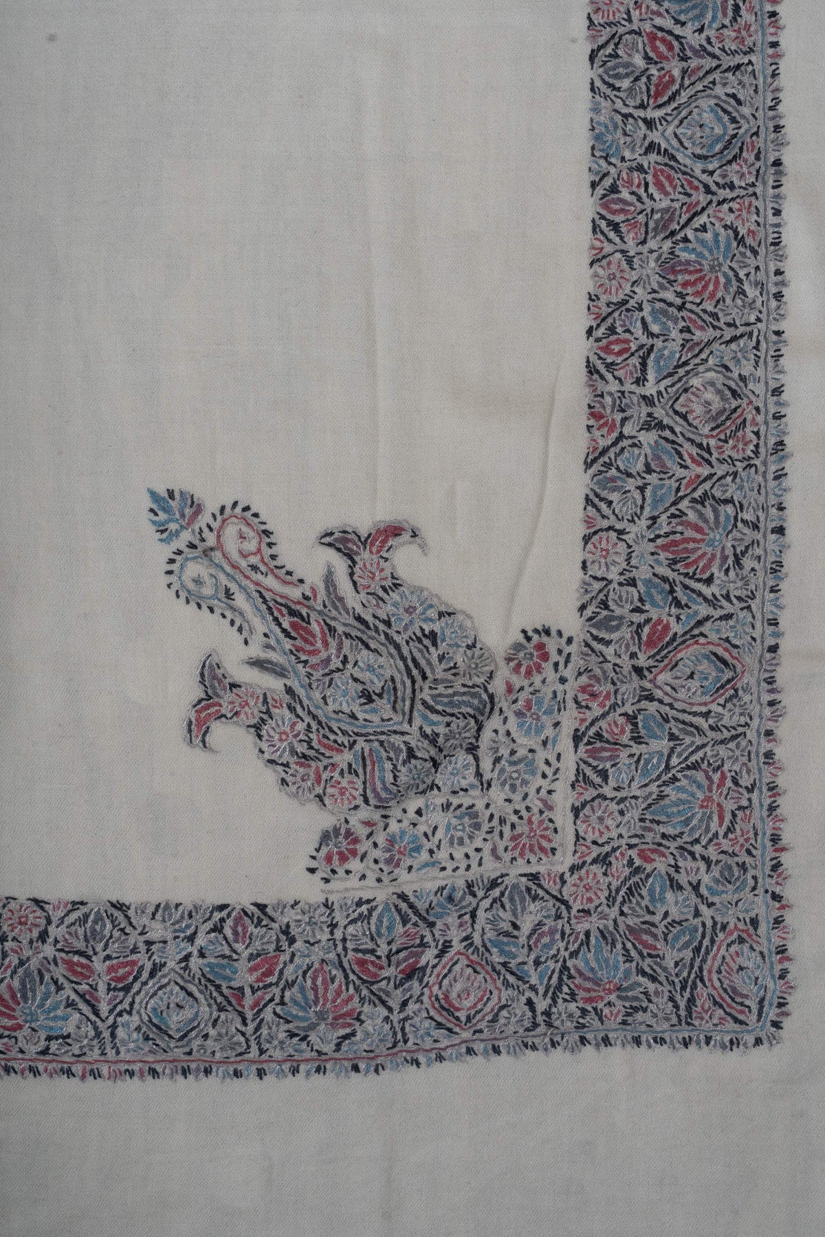 Ivory rumal corner with a large rose-blue floral design rising from the patterned border