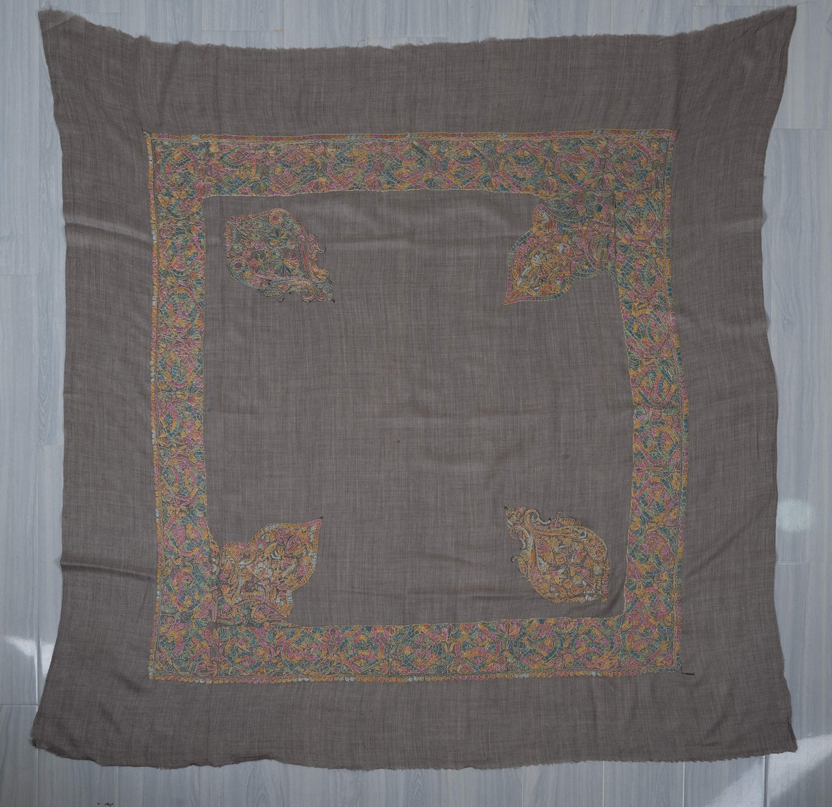 Charcoal square Merino wool rumal laid flat with multicoloured Sozni borders, two separate motifs and two large leafy corners.
