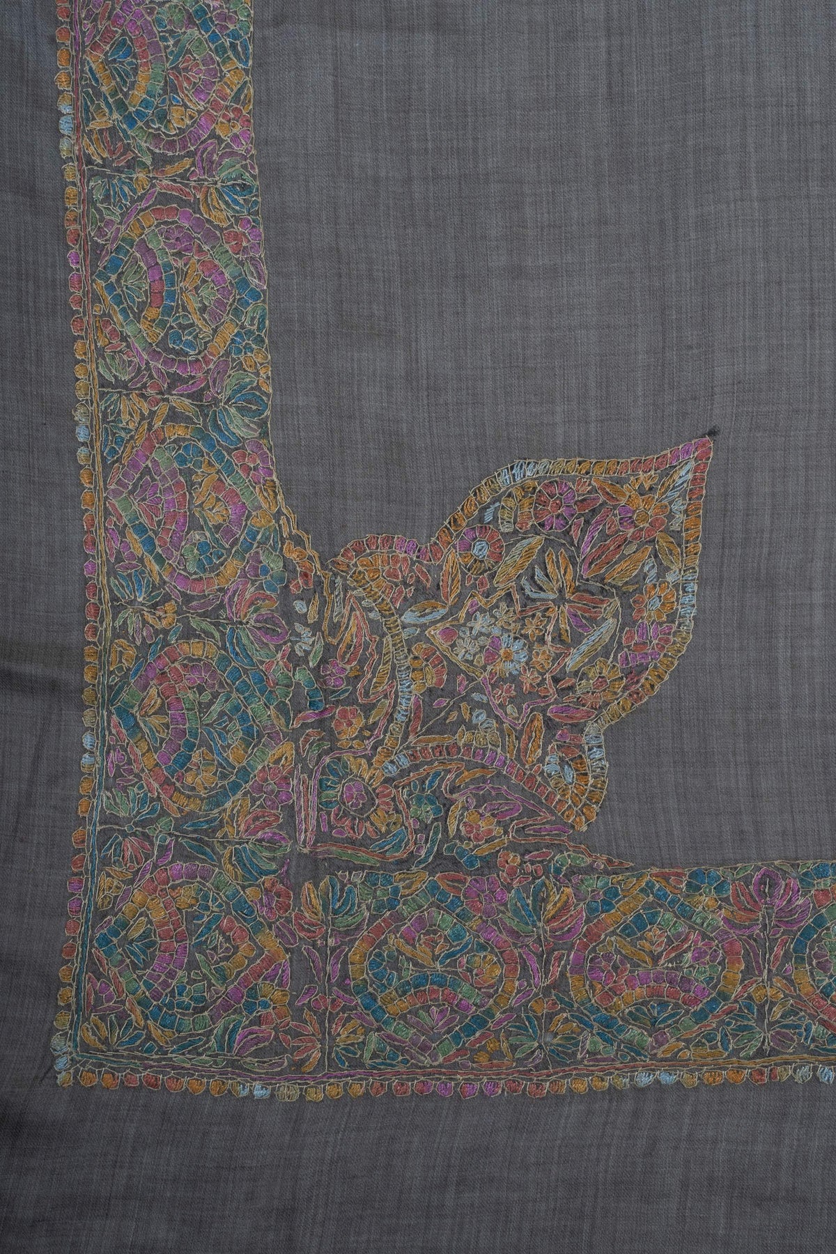 Large multicoloured Sozni flowers and leaves rise from the border at one corner of a charcoal Merino wool rumal.
