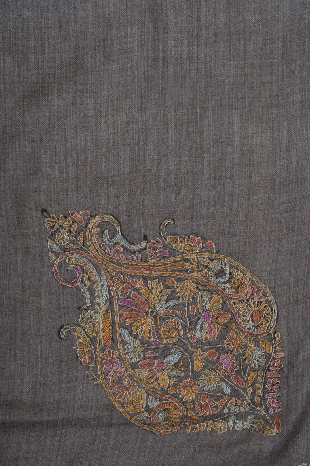 Close-up of an ornate Sozni motif filled with rose, teal and gold flowers and curling stems on charcoal Merino wool.