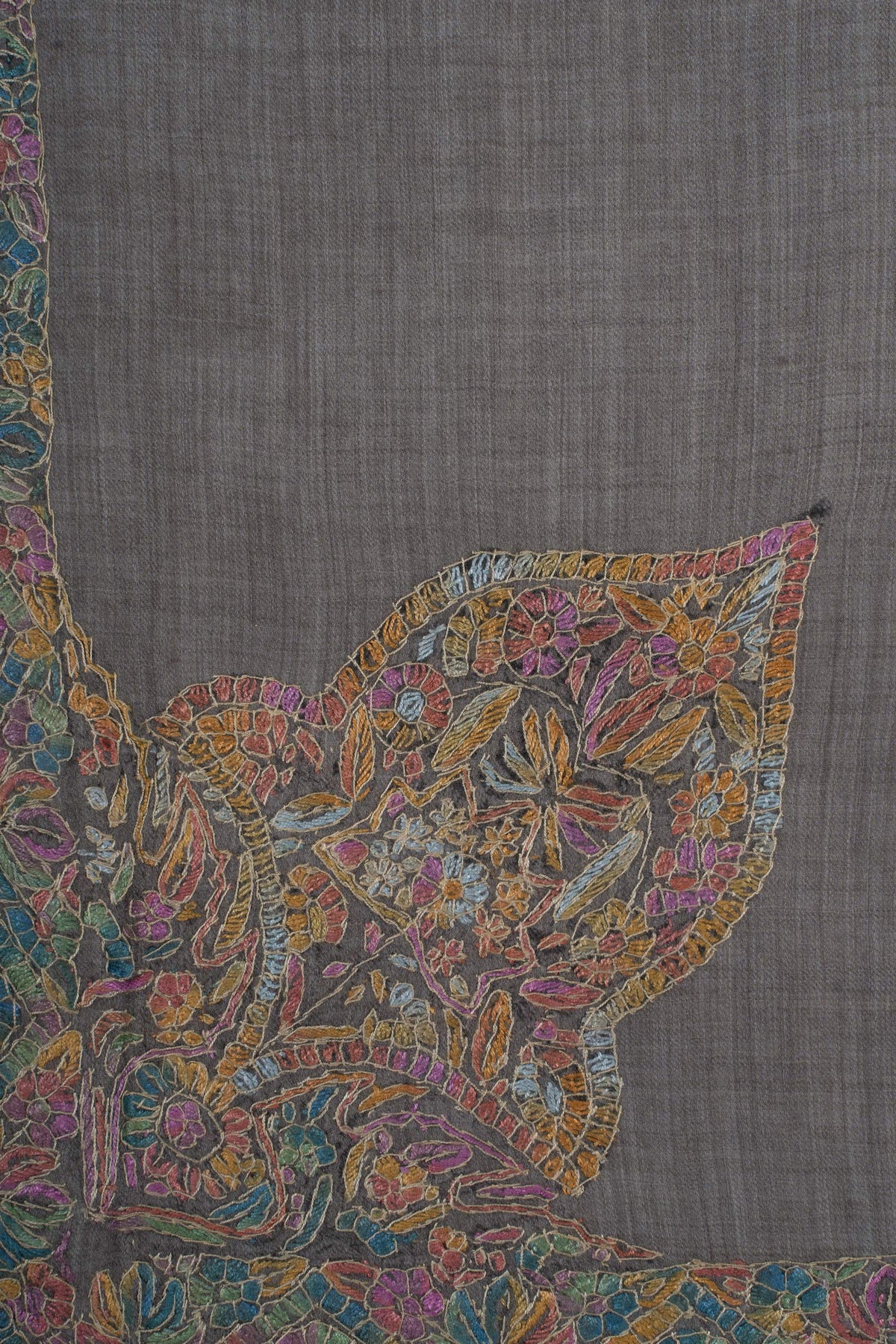 Close-up of a large Sozni corner motif with colourful flowers, leaves and fine gold outlines on charcoal Merino wool.
