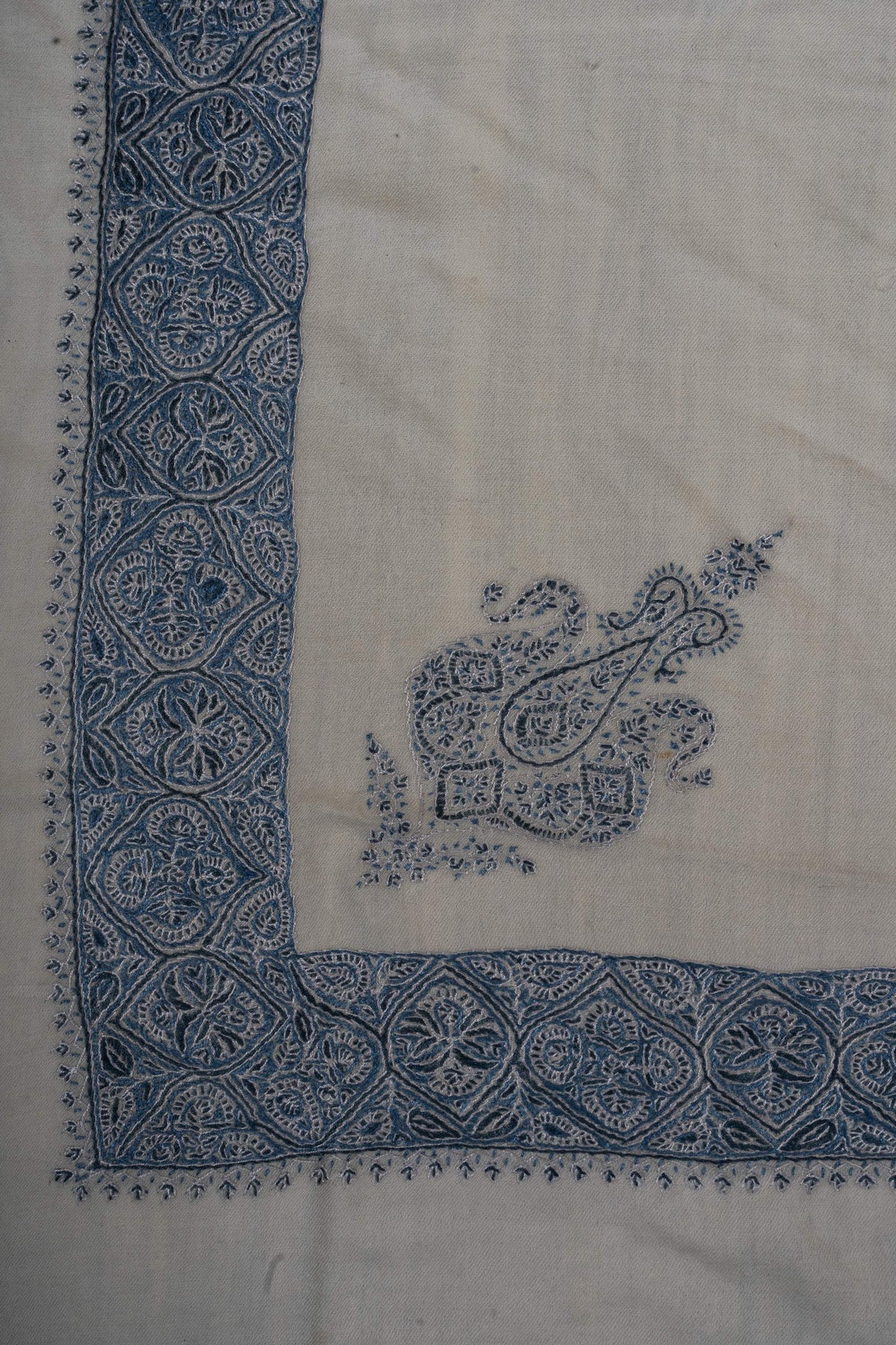 Ivory rumal corner with an indigo paisley crest inside a broad border of floral medallions.