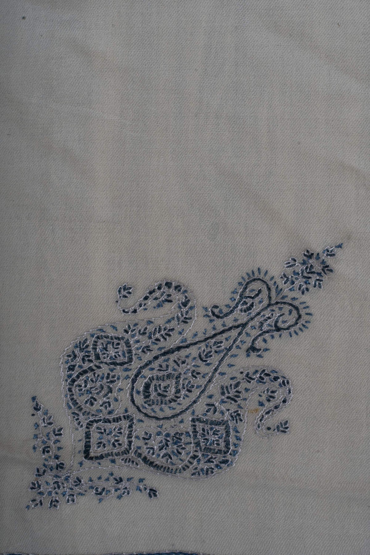Indigo paisley crest surrounded by small flowers and leaves on ivory fabric.