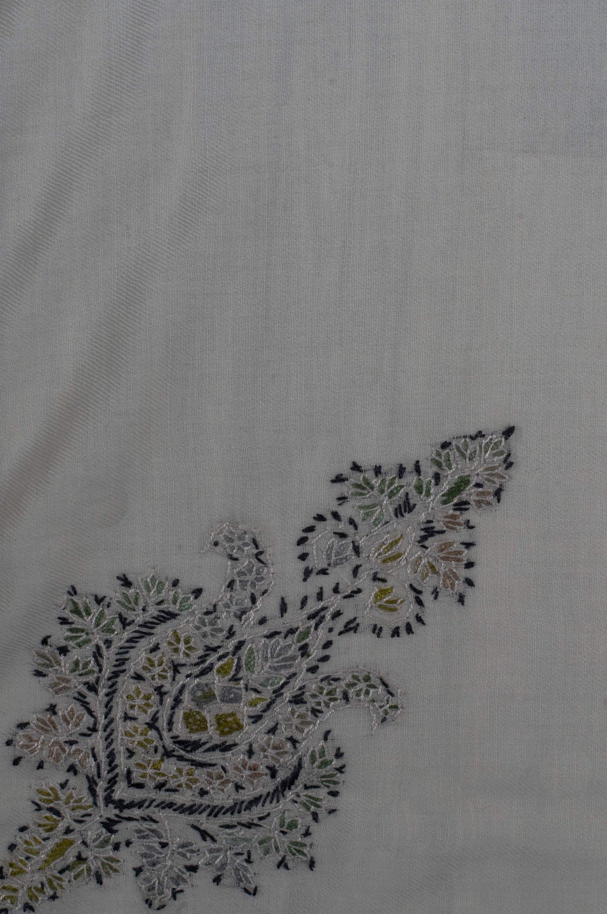Close-up of an olive and charcoal Sozni floral motif with a teardrop centre and delicate leafy sprays on ivory fabric