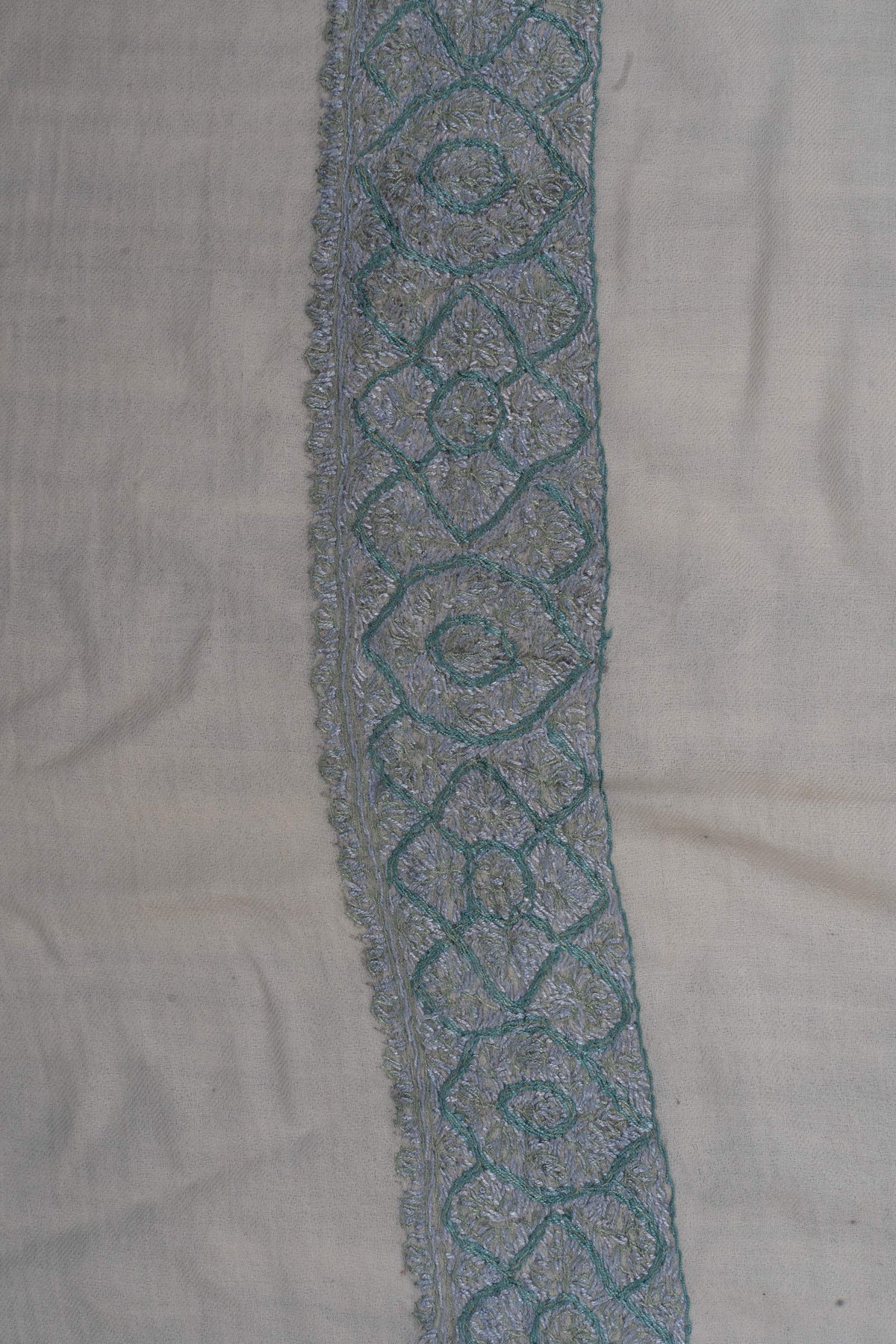 Close-up of the icy-blue embroidered border with repeating looped flowers and oval medallions on ivory fabric.