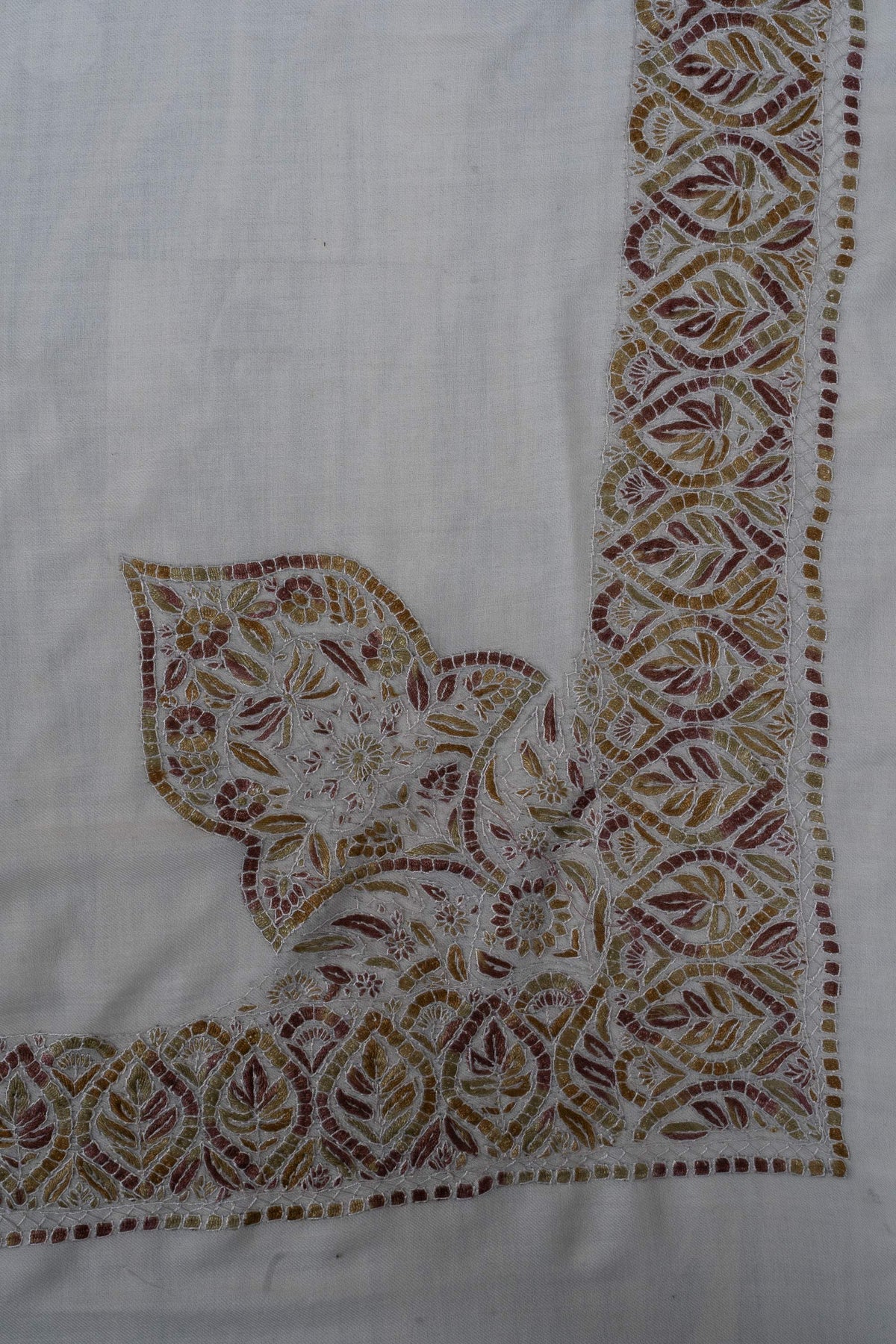 A large Sozni floral leaf motif rises from the amber, olive and rust border at one corner of an ivory Merino wool rumal.