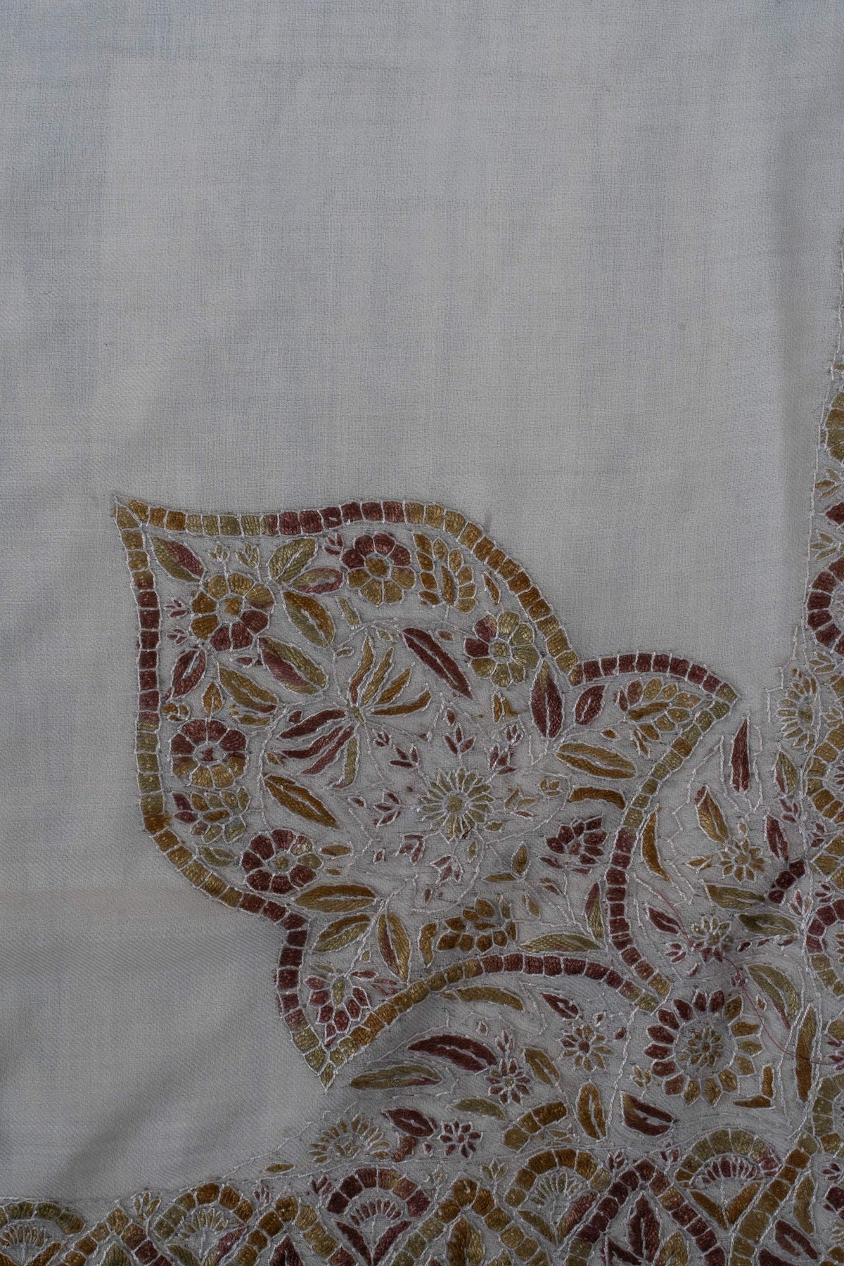 Close-up of a large Sozni corner motif filled with small flowers and leaves in amber, olive and rust on ivory Merino wool.