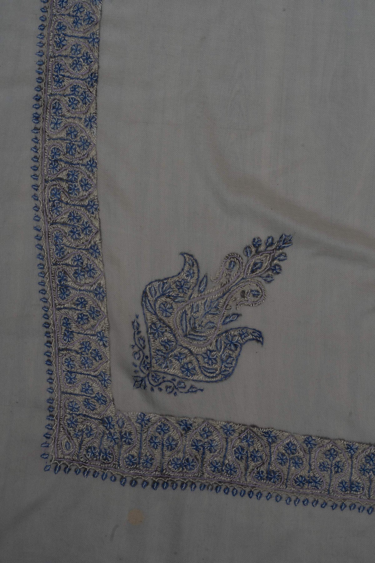 Corner of an ivory Merino wool rumal with a blue Sozni paisley and matching floral borders.
