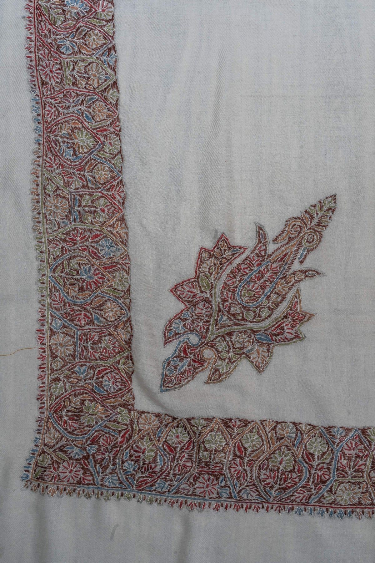 Ivory rumal corner with a detached multicoloured paisley motif inside a densely embroidered floral border.