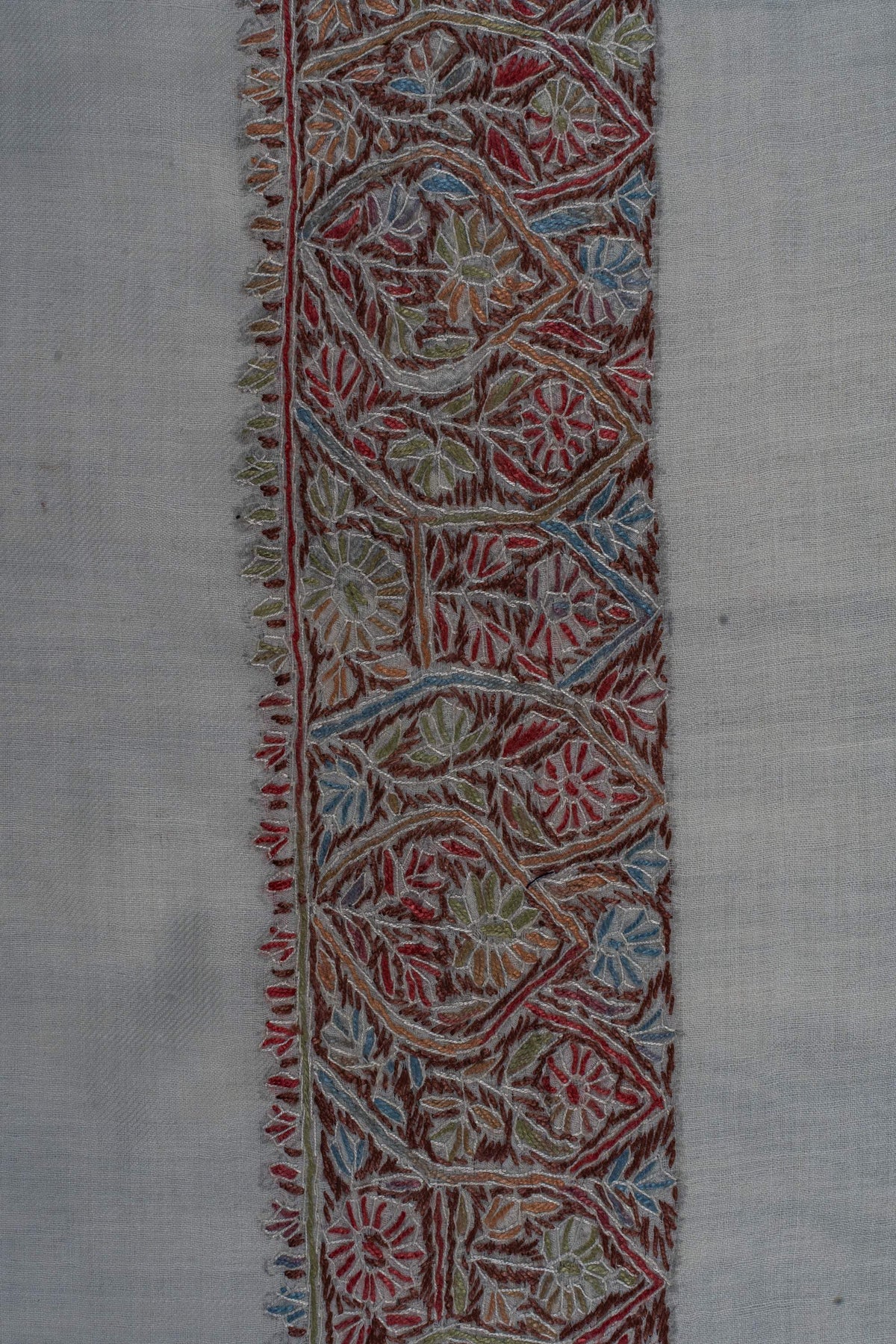 Close-up of the ivory rumal’s dense border with curling leaves and flowers in muted red, green, blue and ochre.