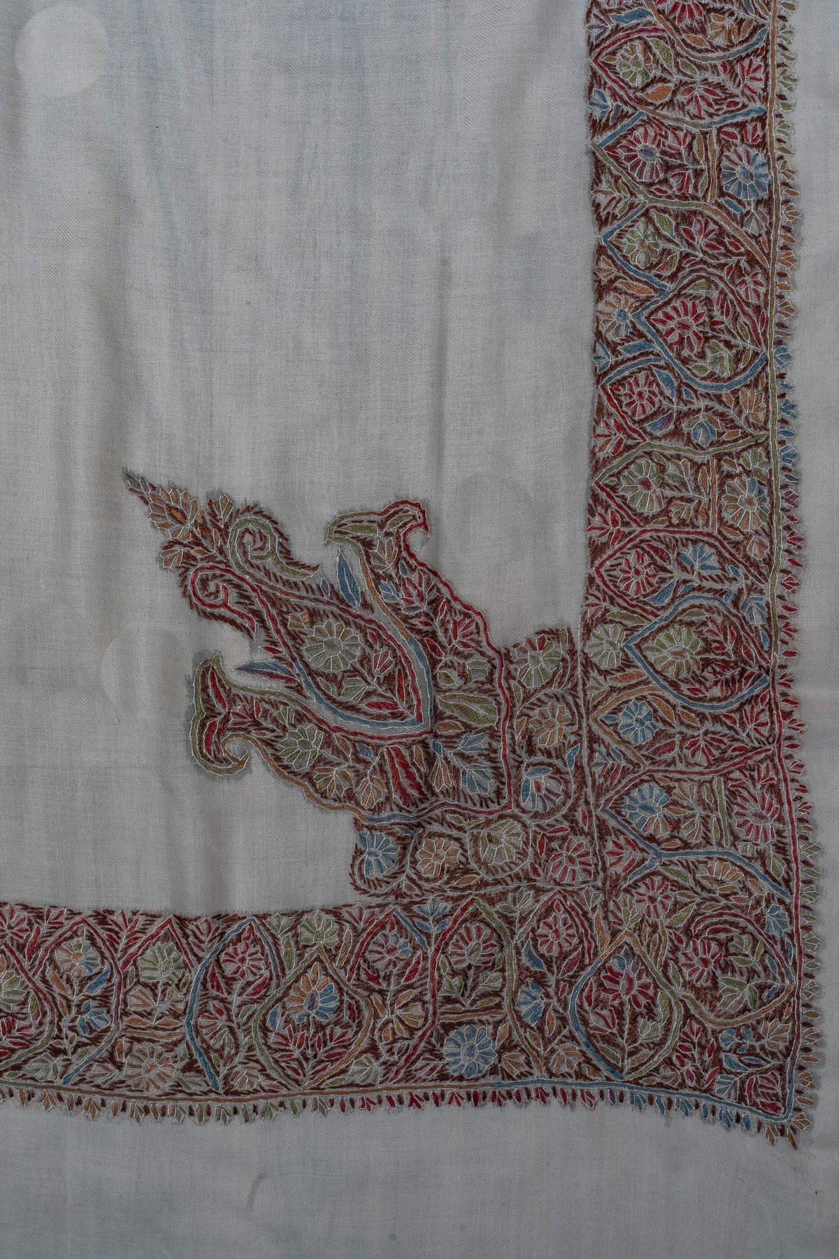 Ivory rumal corner showing a multicoloured paisley motif extending from the floral border.