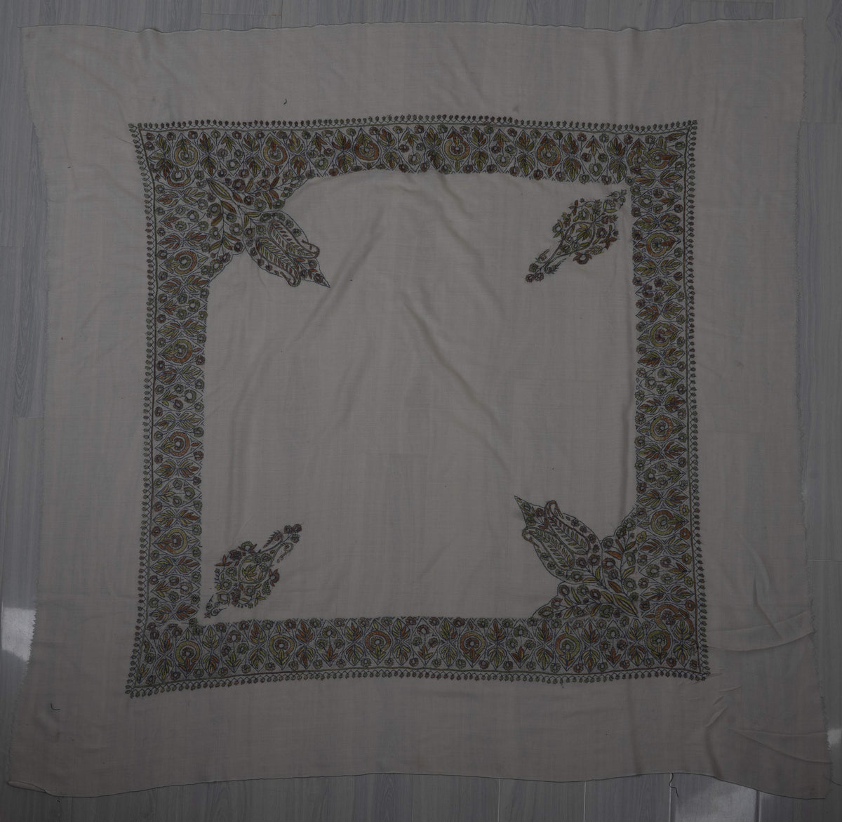 Pale square Merino wool rumal laid flat with sage, blue and ochre Sozni borders, two paisleys and two large leafy corners.