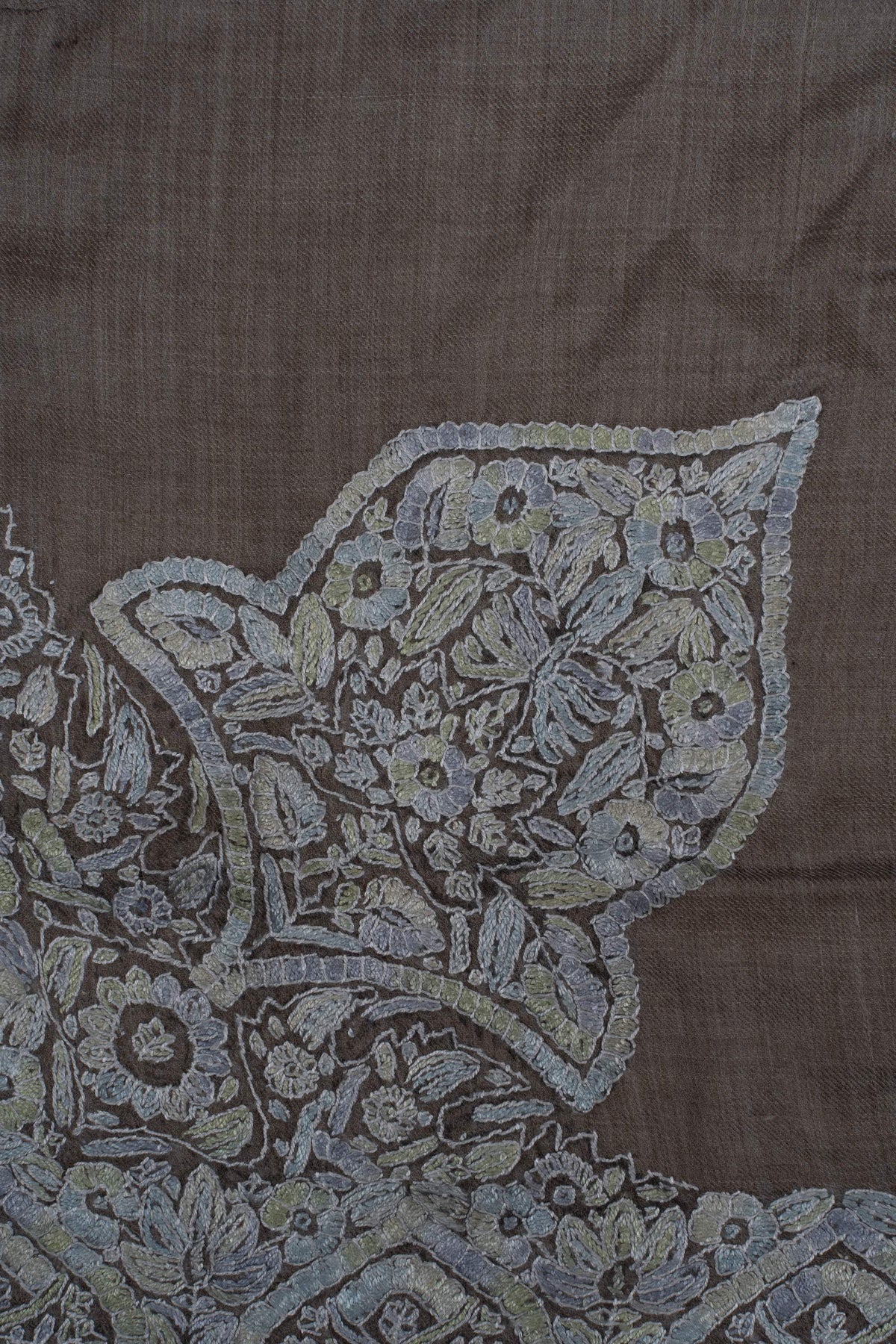 Close-up of a large pale blue-grey Sozni corner panel filled with floral motifs on taupe fabric