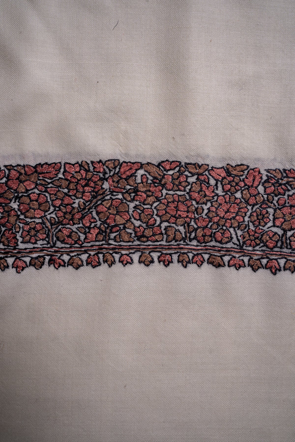 Close-up of muted red Sozni flowers, black outlines and small leaf-shaped edging on ivory Merino wool