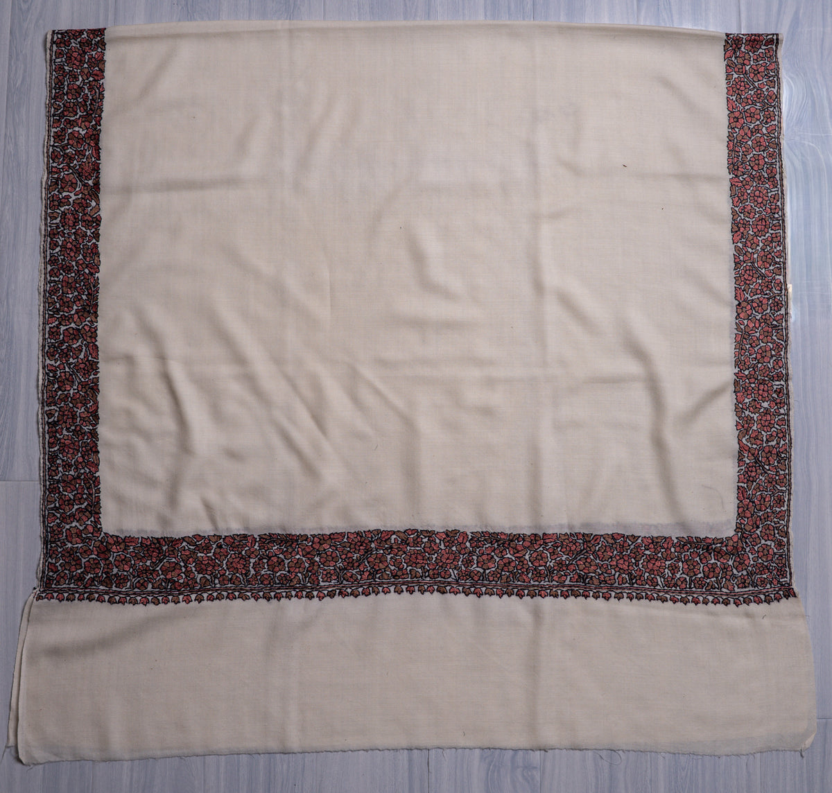 Ivory shawl spread flat with a plain centre and red and black floral Sozni borders along the sides and end