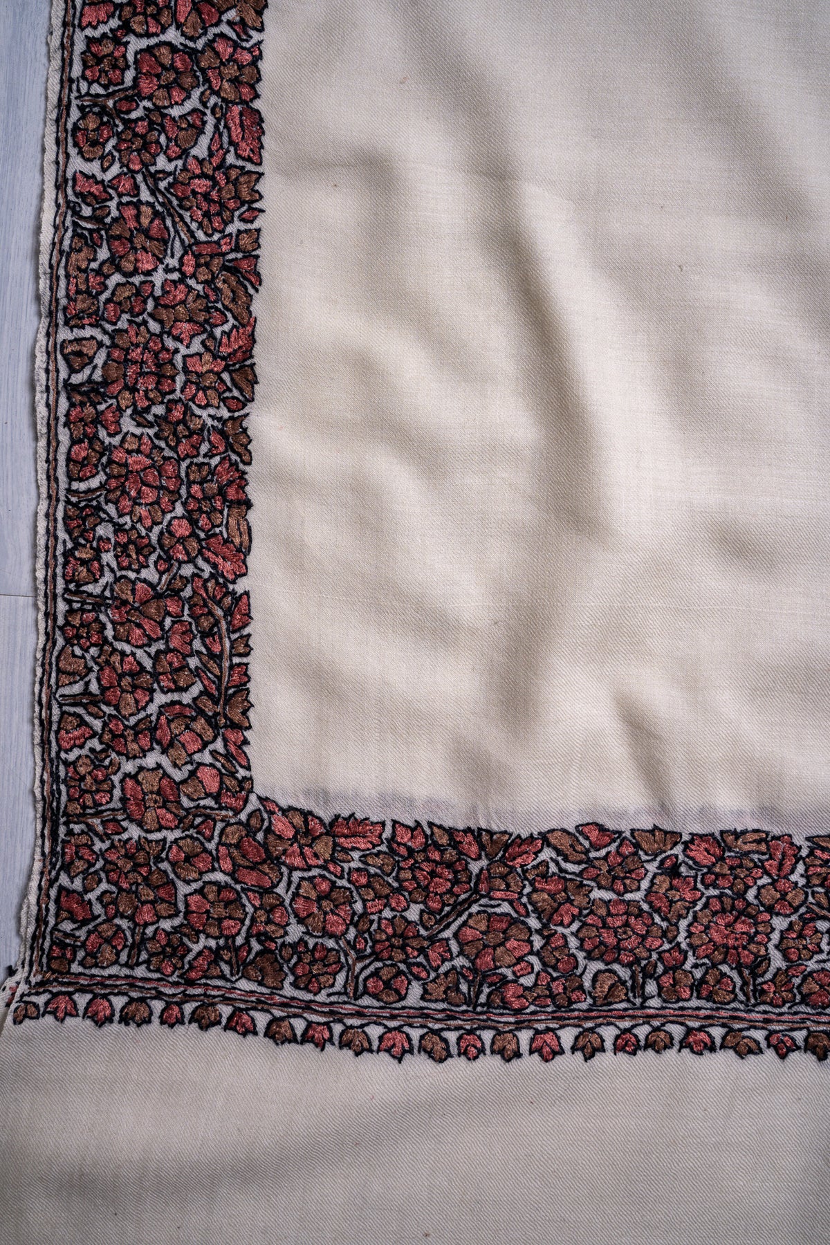 Corner detail of an ivory shawl with muted red flowers and black-outlined Sozni vines