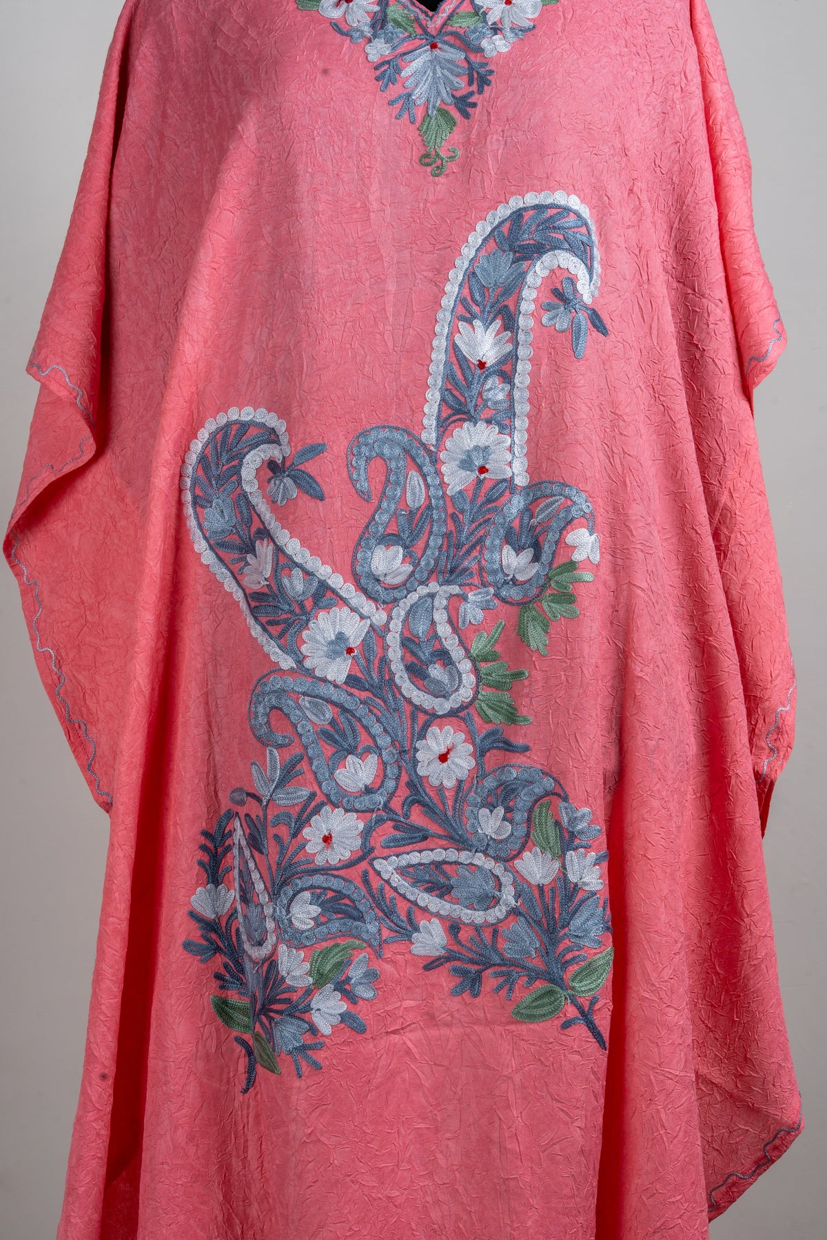 Detail of large blue-and-white paisleys and small flowers across the coral kaftan’s front, with green leaf accents